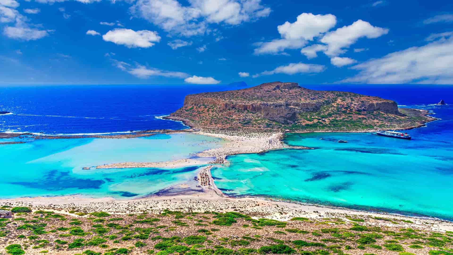 "An aerial shot of Balos Lagoon on Crete's northwest coast, featuring its iconic turquoise water, pink sand beach, and the rugged Gramvousa Island. "