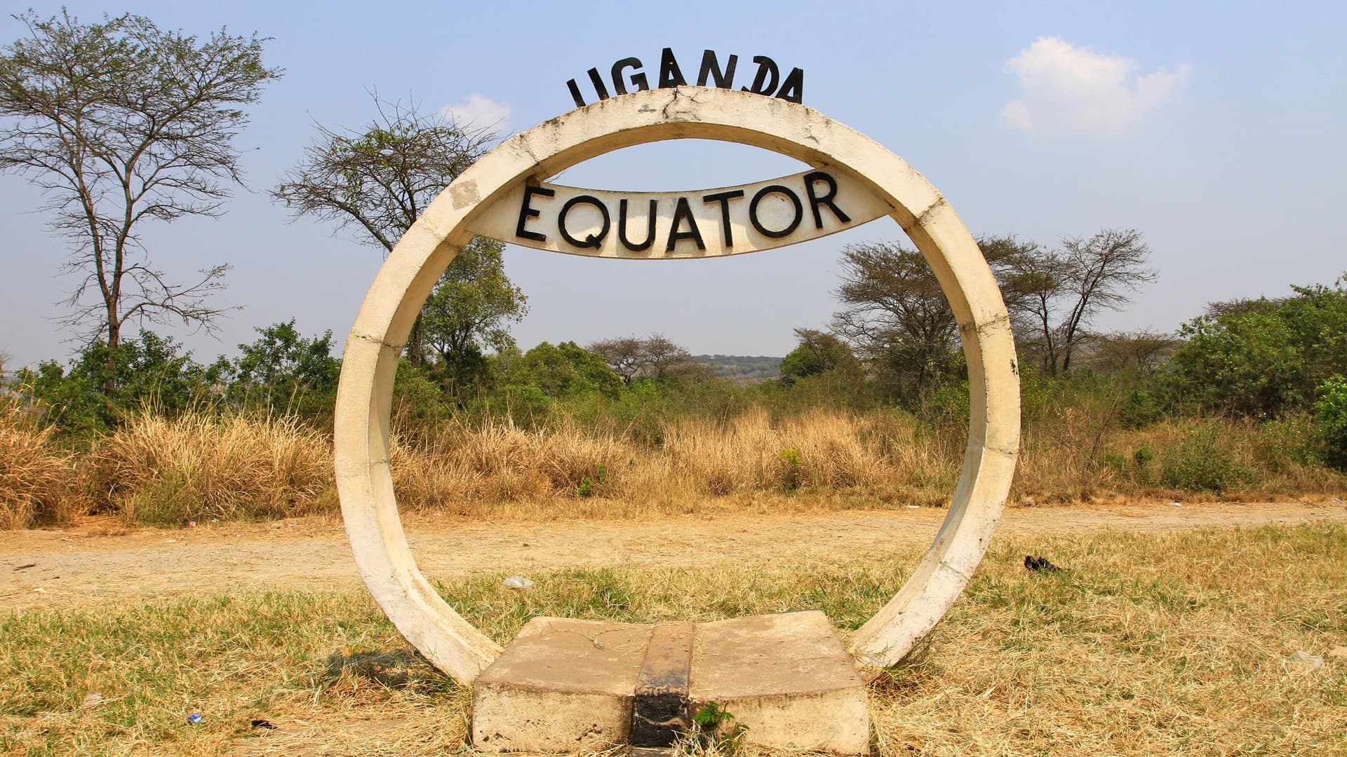A prominent circular monument marks the Equator in Uganda, featuring the word "EQUATOR" and "UGANDA" with a grassy landscape in the background.