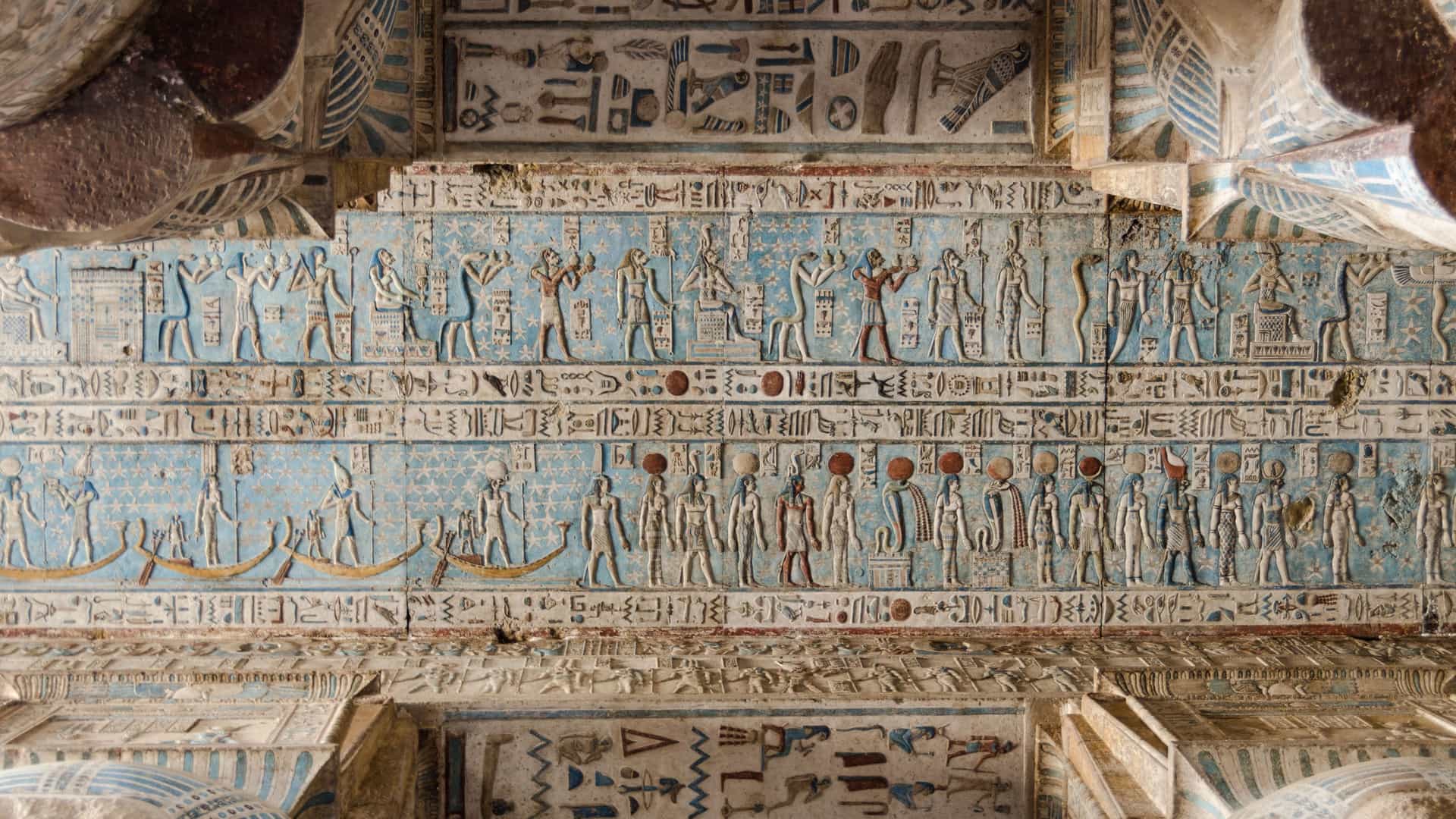 A detailed view of the well-preserved hieroglyphic wall carvings and painted reliefs depicting gods and boats inside the Dendera Temple in Egypt.