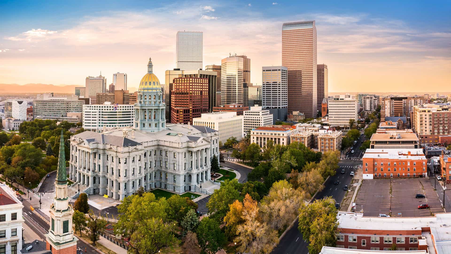 "A stunning panoramic shot of the Denver, Colorado, skyline, with the majestic gold-domed State Capitol building in the foreground and modern skyscrapers rising behind it, set against a beautiful sunset sky. "