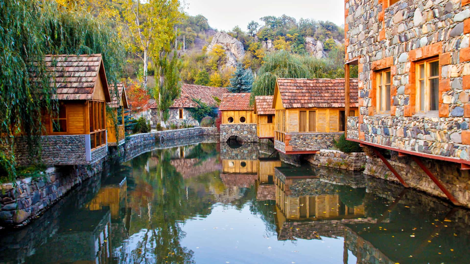 A scenic view of historic houses with stone and wooden facades, their terracotta roofs reflecting in the calm river that flows through the heart of the Dilijan, Armenia, a beautiful and tranquil town.