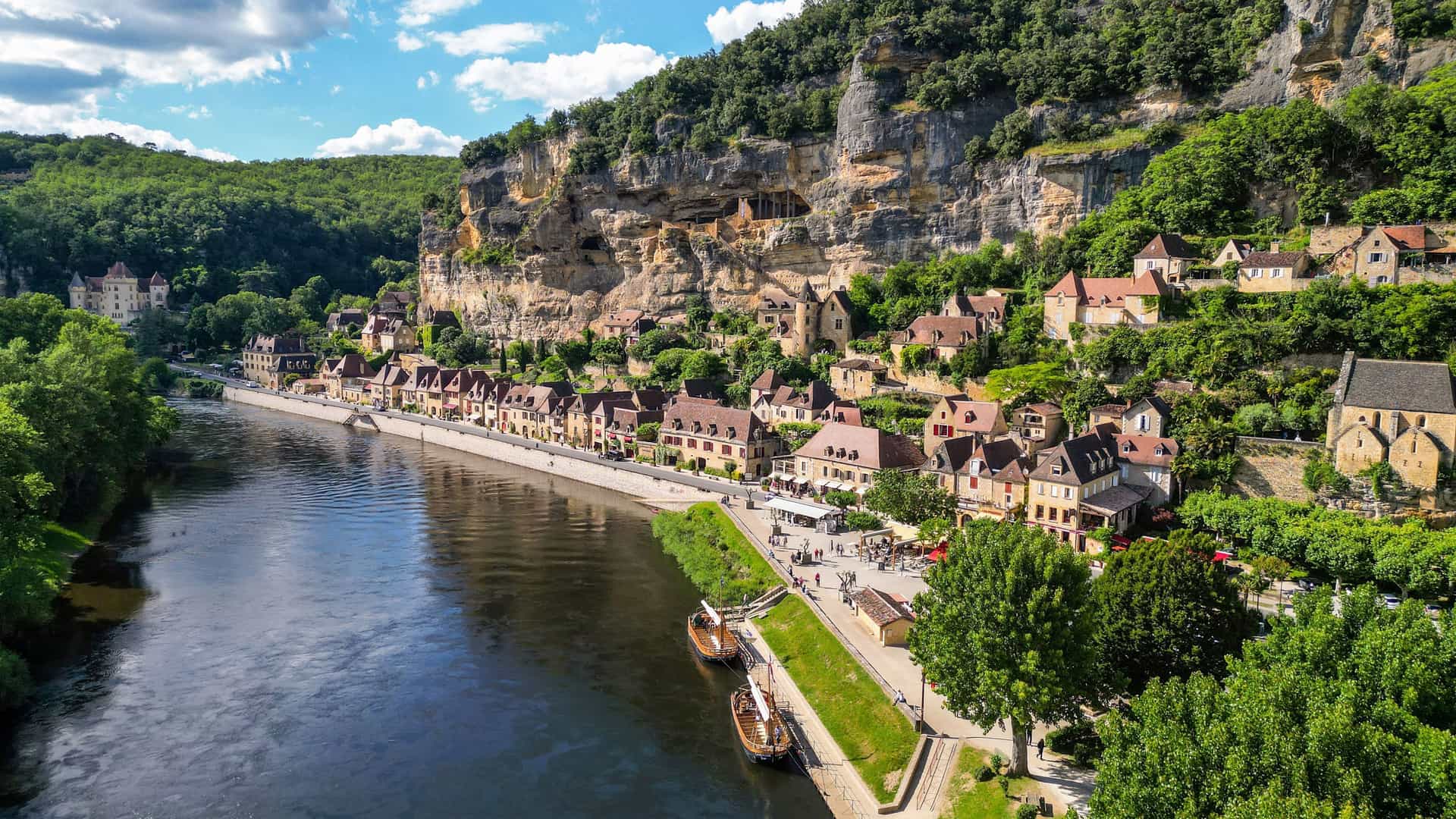 The stunning medieval village of La Roque-Gageac, France, nestled between the tranquil Dordogne River and a dramatic, towering cliff face.