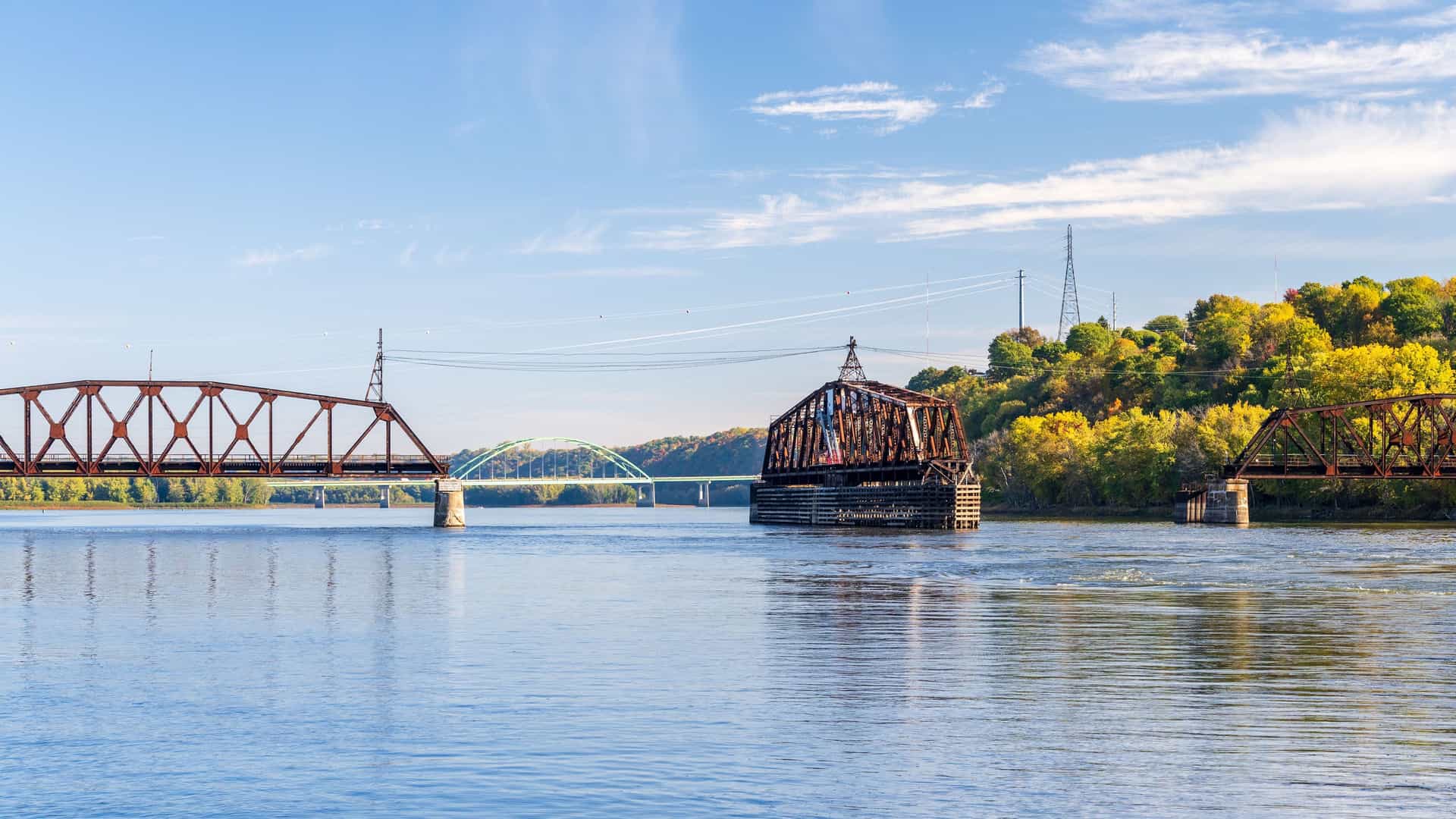 A view of the historic railroad and Julien Dubuque bridges spanning the Mississippi River, with lush autumn foliage on the banks of Dubuque, Iowa.