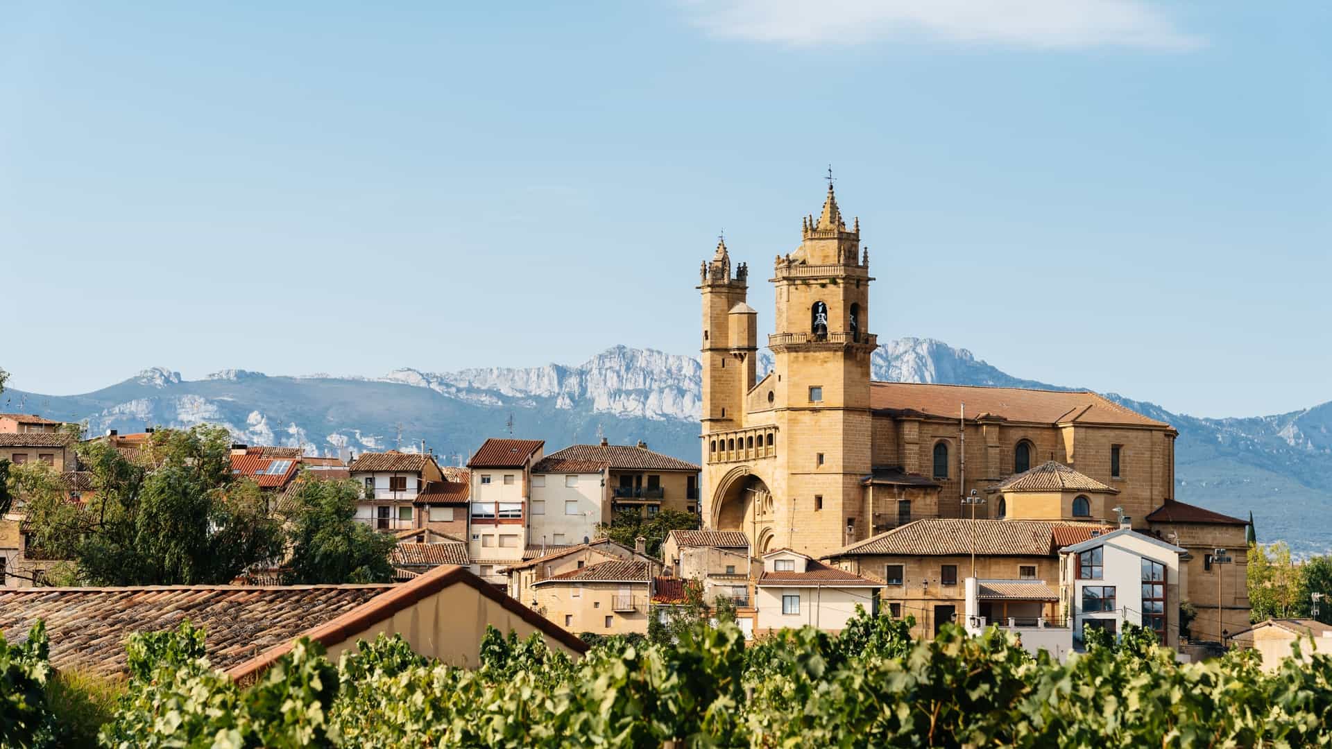 The bell towers of San Andrés Church overlooking the rooftops of Elciego, Spain. Vineyards frame the town and the Cantabrian Mountains.