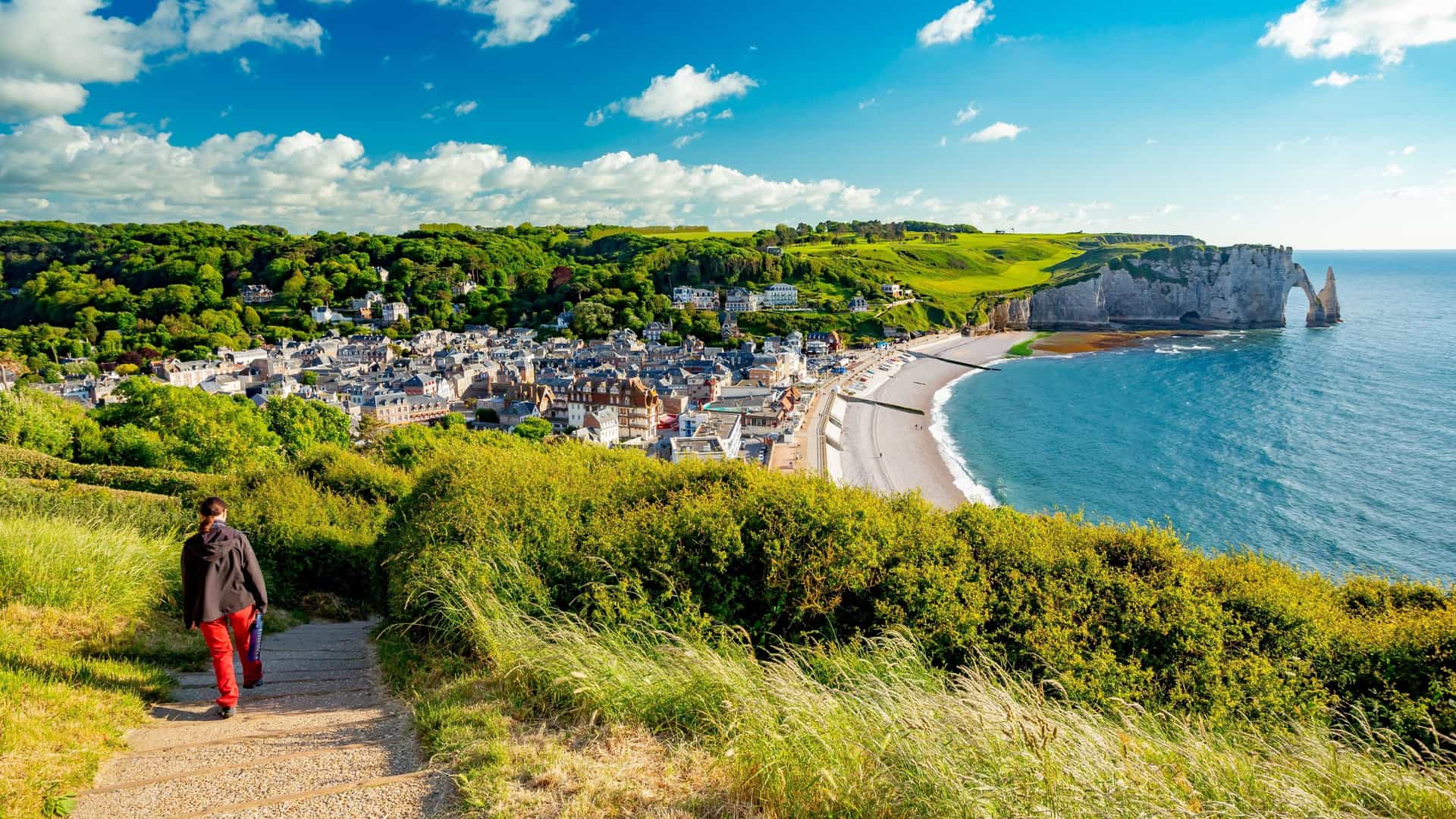 Scenic view of the village of Étretat, France, from a high viewpoint, showing the beach, white chalk cliffs, and the famous Manneporte arch on the Alabaster Coast of Normandy.