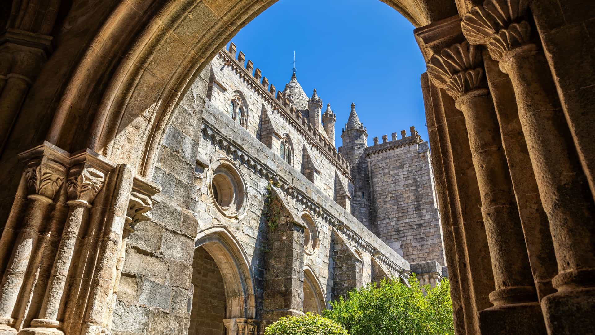 "A view from inside a stone archway of the historic Évora Cathedral in Portugal, with its robust Gothic architecture and a clear blue sky in the background. "