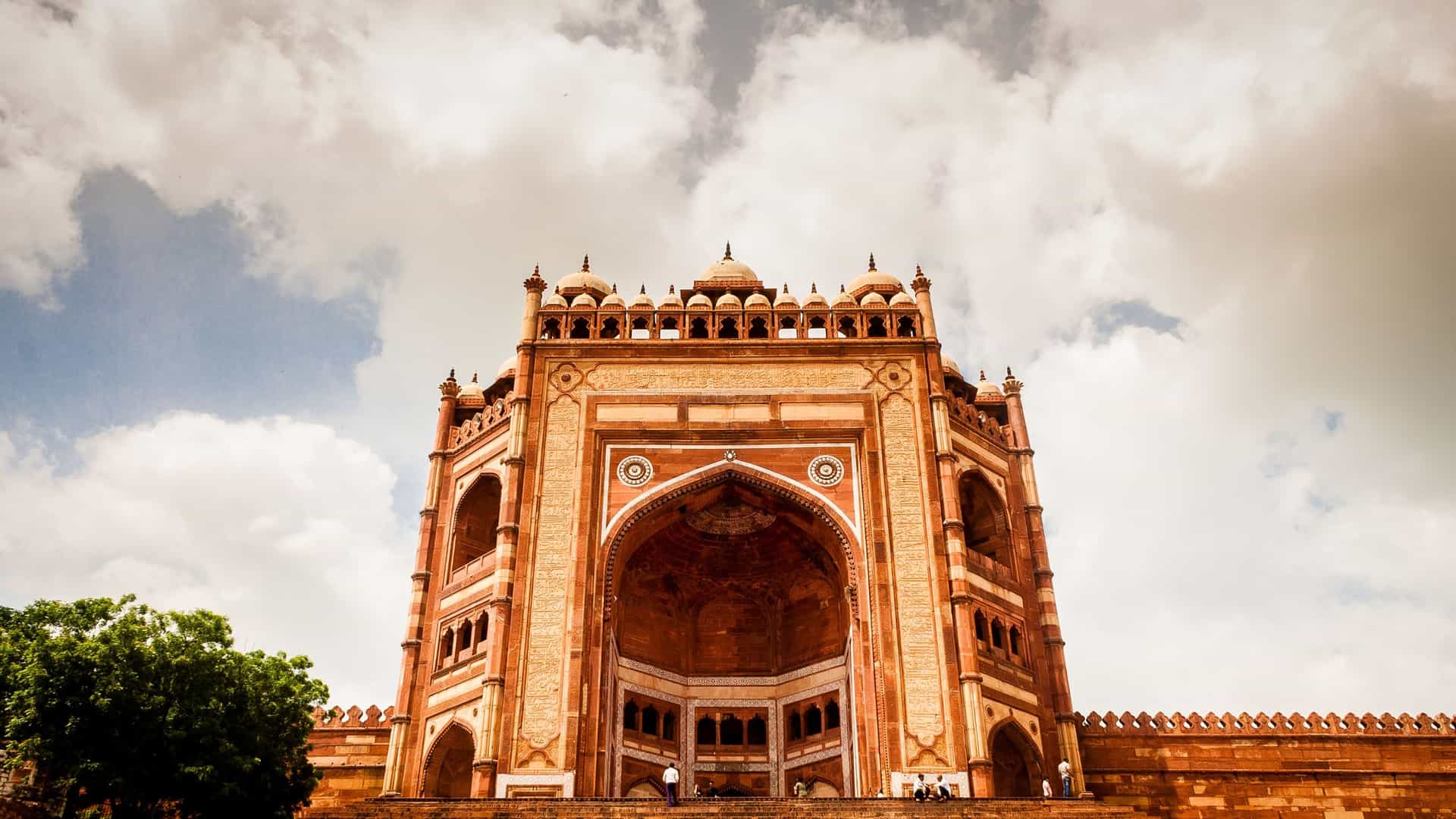 A low-angle shot of the magnificent Buland Darwaza, the monumental gateway to the Fatehpur Sikri complex in Agra, India, showcasing its ornate red sandstone architecture against a cloudy sky.