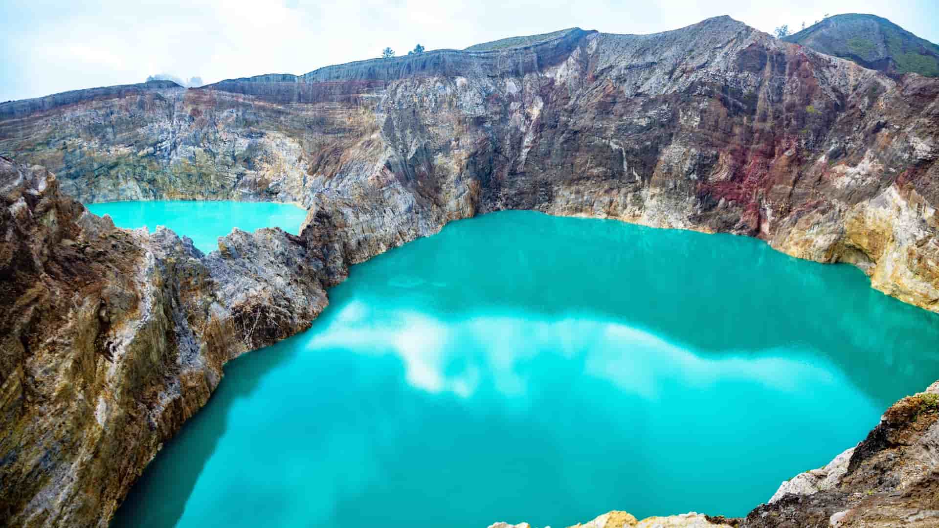 The intensely turquoise-colored water of two adjacent Kelimutu crater lakes (Tiwi Ata Mbupu and Tiwu Nuwa Muri Koo Fai) on Flores Island, Indonesia, surrounded by rugged volcanic rock.