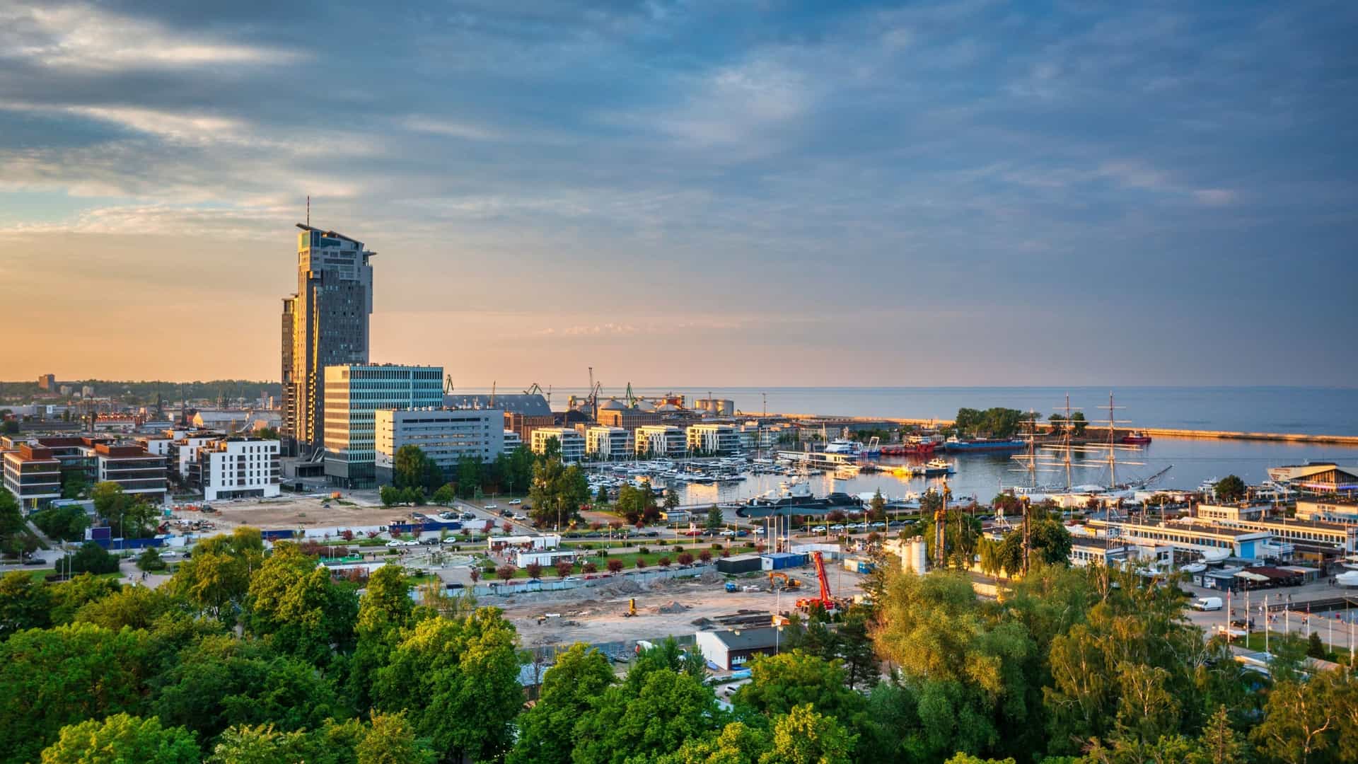 The modern skyline and harbor of Gdynia, Poland, seen at sunset, with a prominent skyscraper and marina.