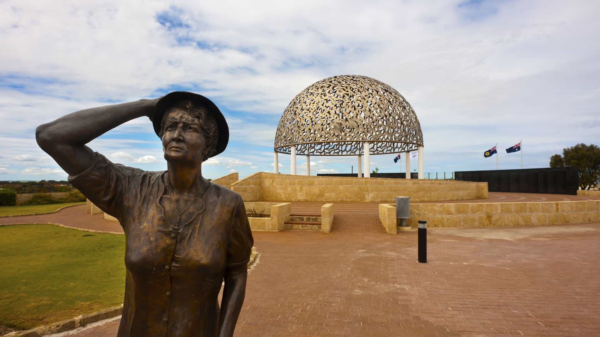 A close-up of the HMAS Sydney II Memorial in Geraldton, Australia, featuring the "Waiting Woman" bronze statue with the dome of 645 stainless steel seagulls in the background.