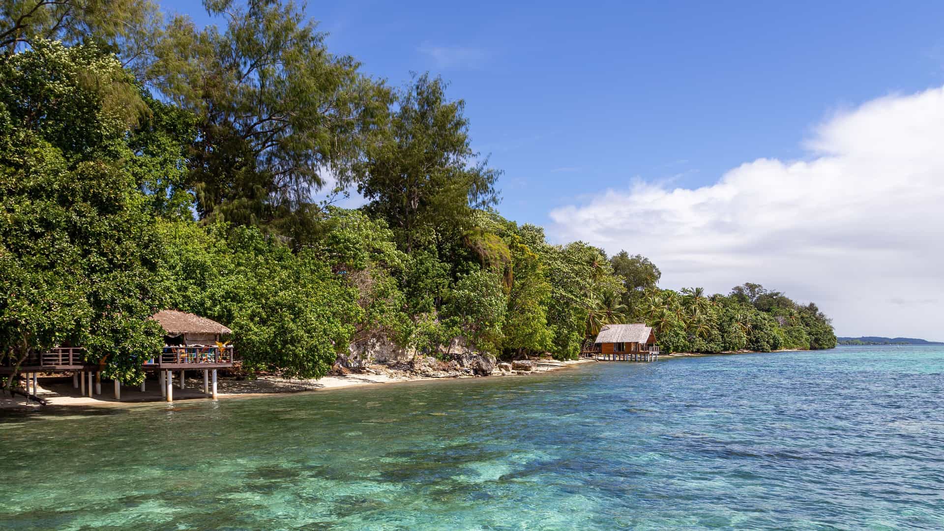 A serene tropical landscape of Gizo Island in the Solomon Islands, showcasing a calm, turquoise ocean, a sandy beach, lush green trees, and two rustic overwater bungalows.