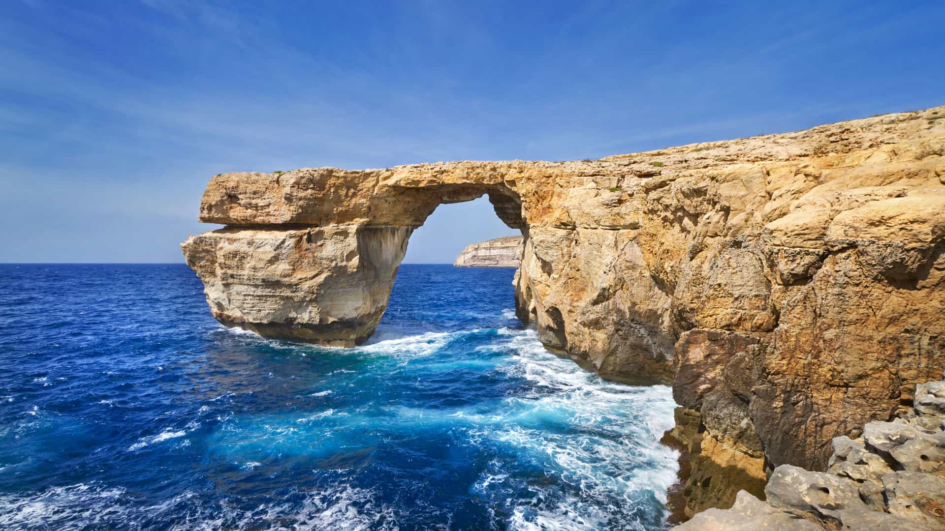 A beautiful landscape of the iconic Azure Window, a natural rock archway in Gozo, Malta, with powerful blue waves crashing below the massive cliffs.