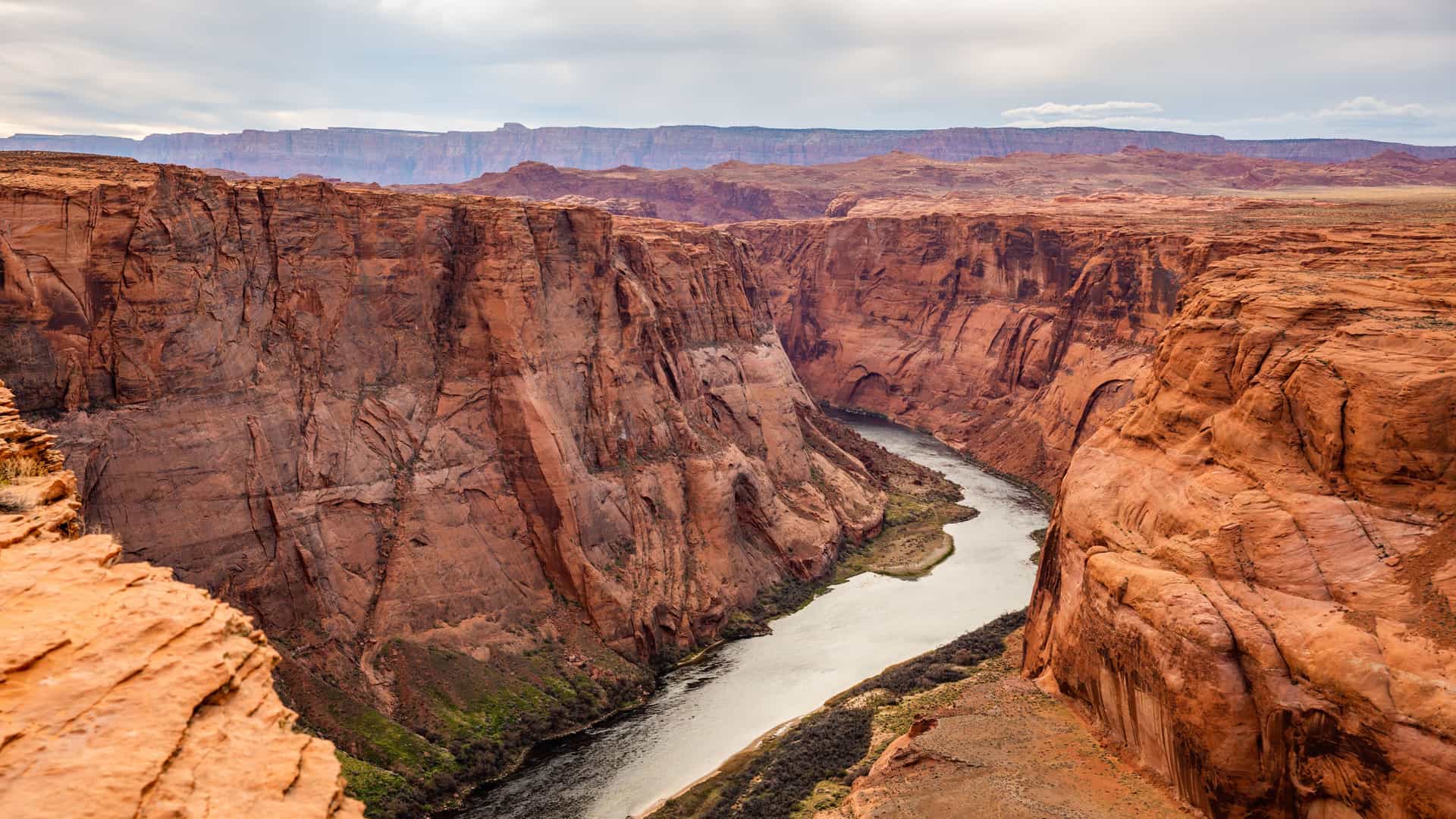 "A high-angle view of the iconic Horseshoe Bend at the Grand Canyon National Park, showcasing the Colorado River's sharp turn through the deep red and orange rock formations. "