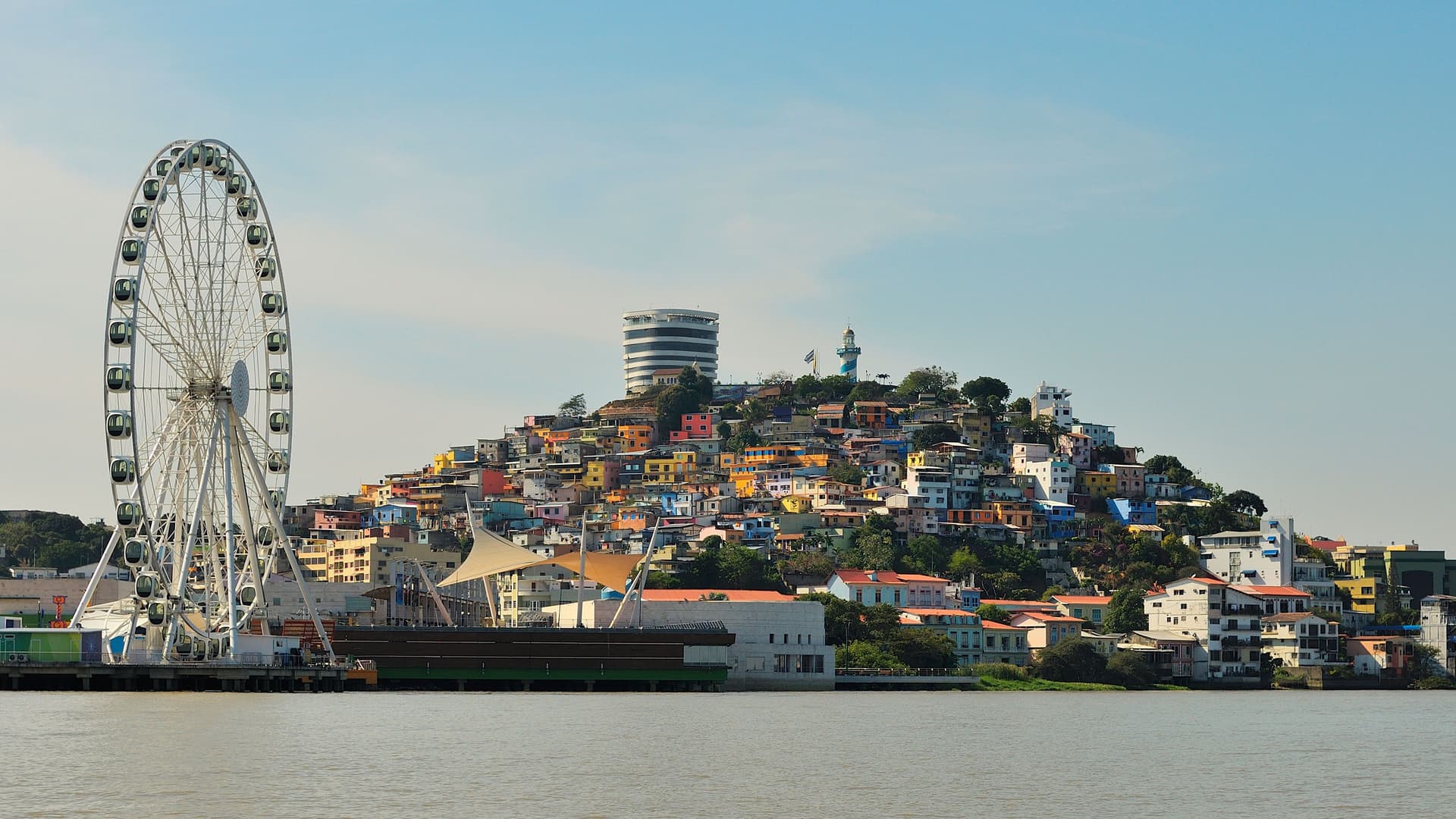 The vibrant, colorful houses of Santa Ana Hill and the massive La Perla Ferris wheel along the waterfront of the Guayas River in Guayaquil, Ecuador.