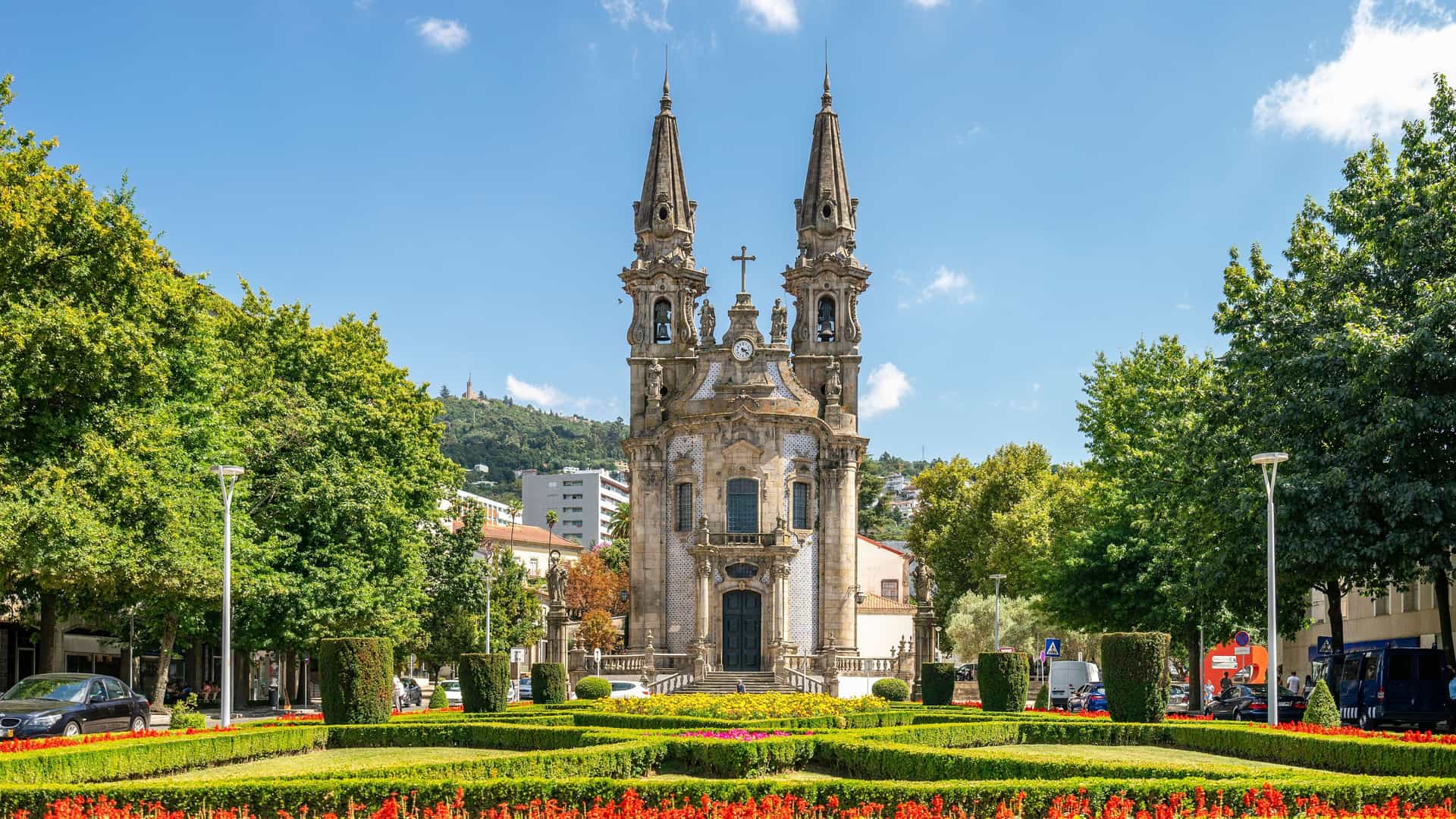 The beautiful twin-steeple Igreja e Convento de São Francisco church in Guimarães, Portugal, surrounded by a meticulously manicured garden and lush green trees.