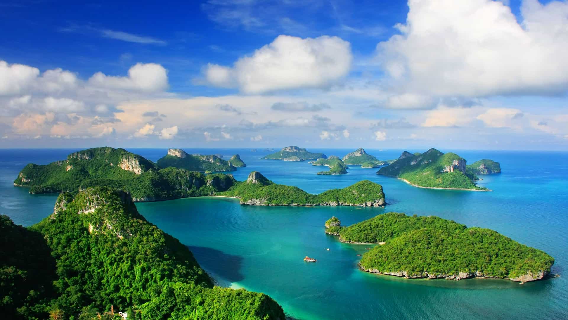 A beautiful aerial shot of the Gulf of Thailand, showcasing a cluster of lush, green islands and turquoise water under a blue sky with fluffy clouds.