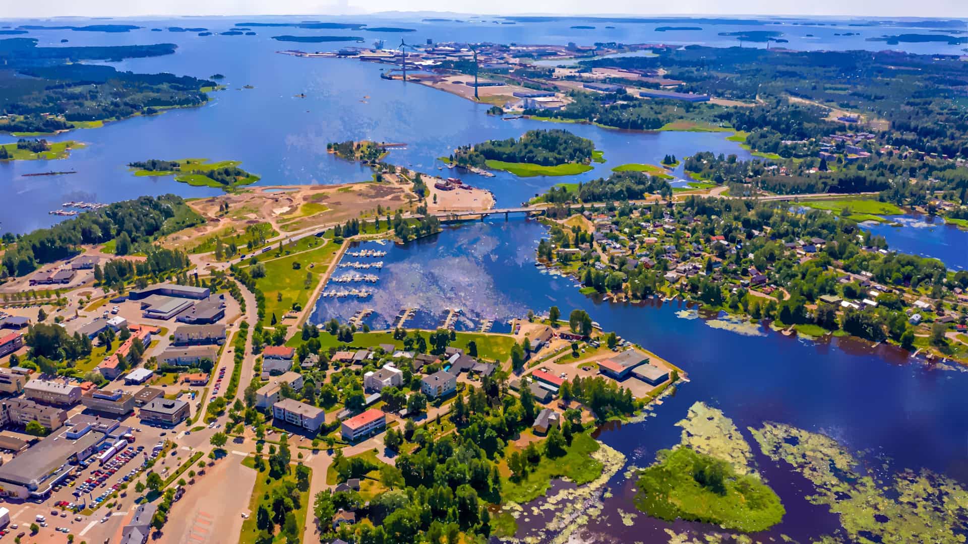An aerial view of Hamina, Finland, showcasing a scenic bay with a large port, several small islands, and a residential area with a marina and harbor.
