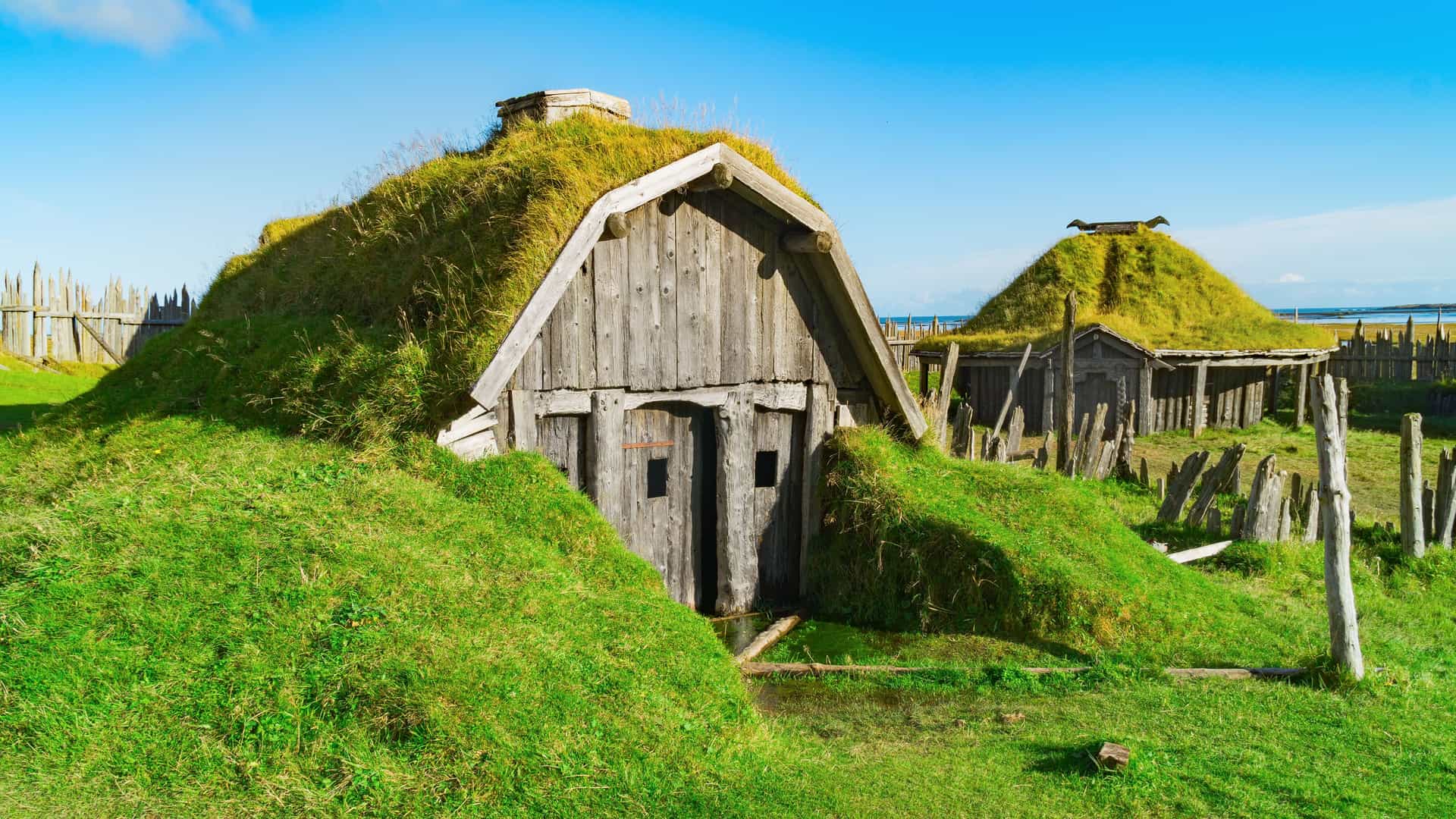 "A close-up view of the historic Viking village set with traditional turf-roofed houses near Höfn, Iceland, with weathered wooden fronts and lush grass roofs. "