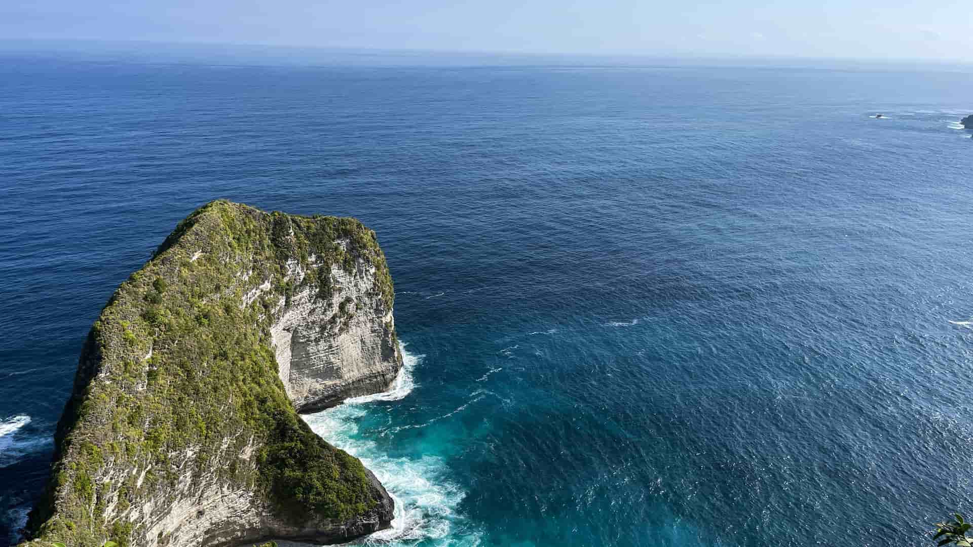 A dramatic aerial shot of the rugged coastline of the Indian Ocean, with a large, green, jagged cliff jutting out into the deep blue water.