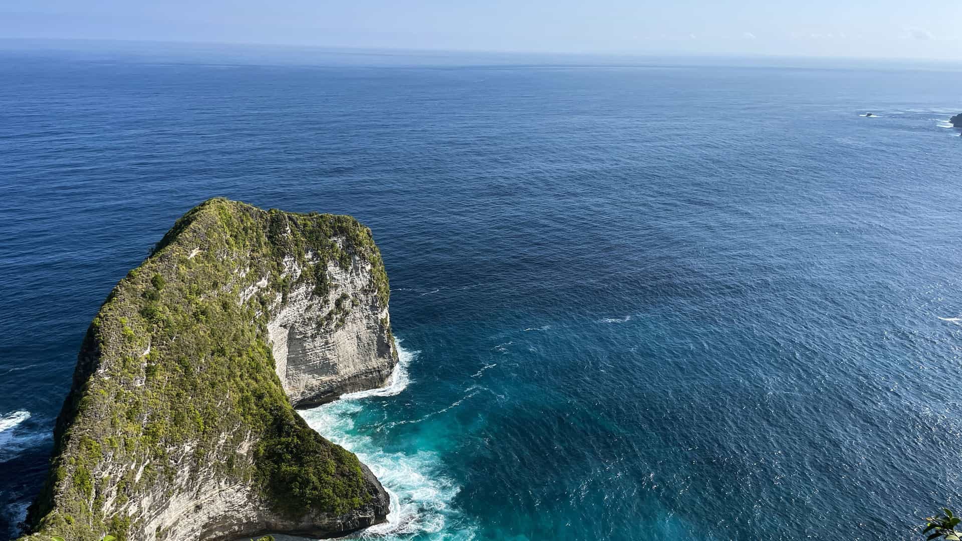 A dramatic aerial shot of the rugged coastline of the Indian Ocean, with a large, green, jagged cliff jutting out into the deep blue water.