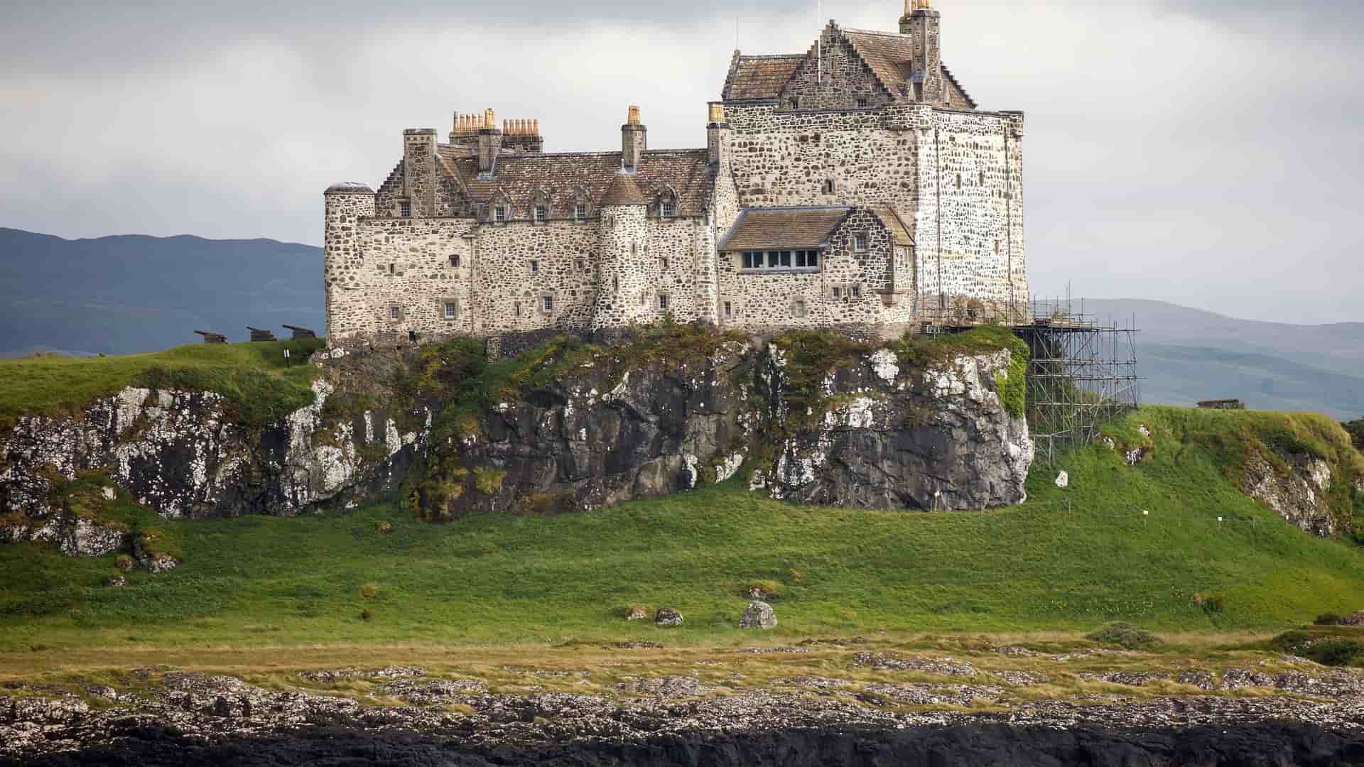 A scenic shot of Duart Castle, a historic stone fortress with a rugged exterior, situated on a green cliff overlooking the sea on the Isle of Mull.