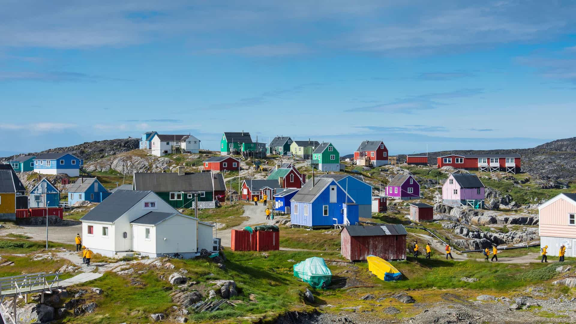 A panoramic view of the remote village of Itilleq in Greenland, with its brightly colored wooden houses scattered across the rocky, green landscape.