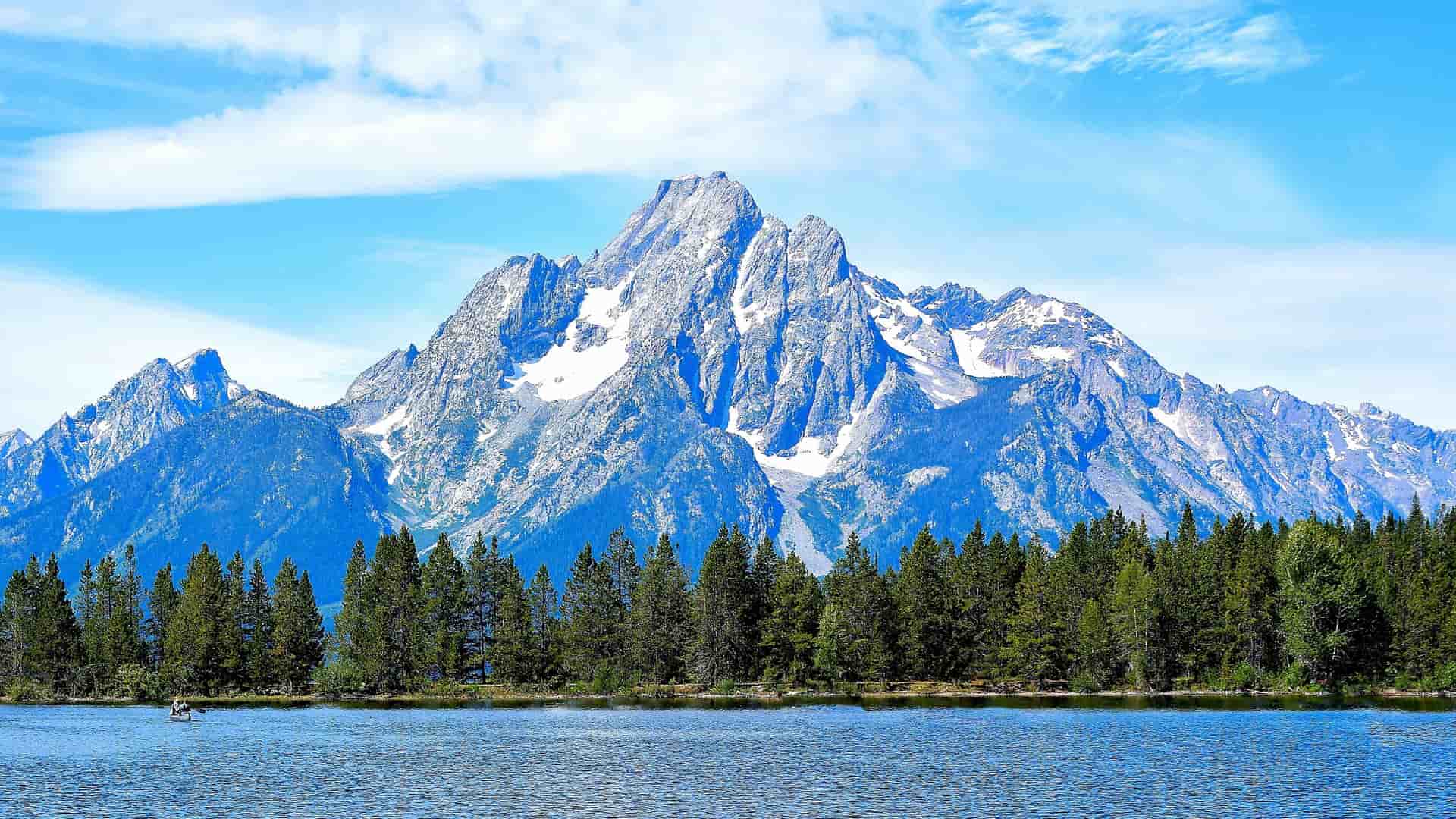 Snow-capped mountains of the Teton Range rise above a line of forest and a lake in Jackson Hole, Wyoming.