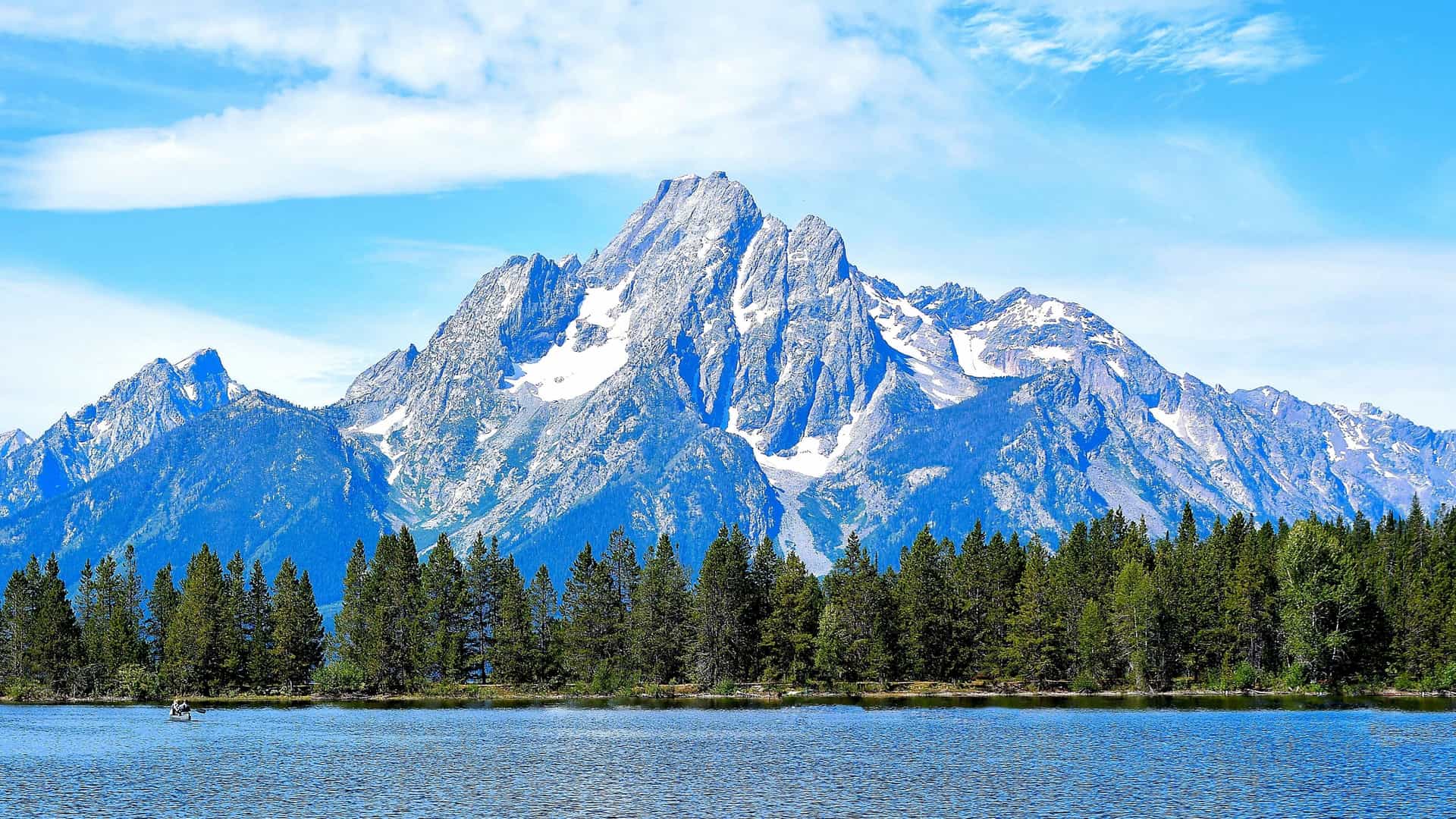 Snow-capped mountains of the Teton Range rise above a line of forest and a lake in Jackson Hole, Wyoming.