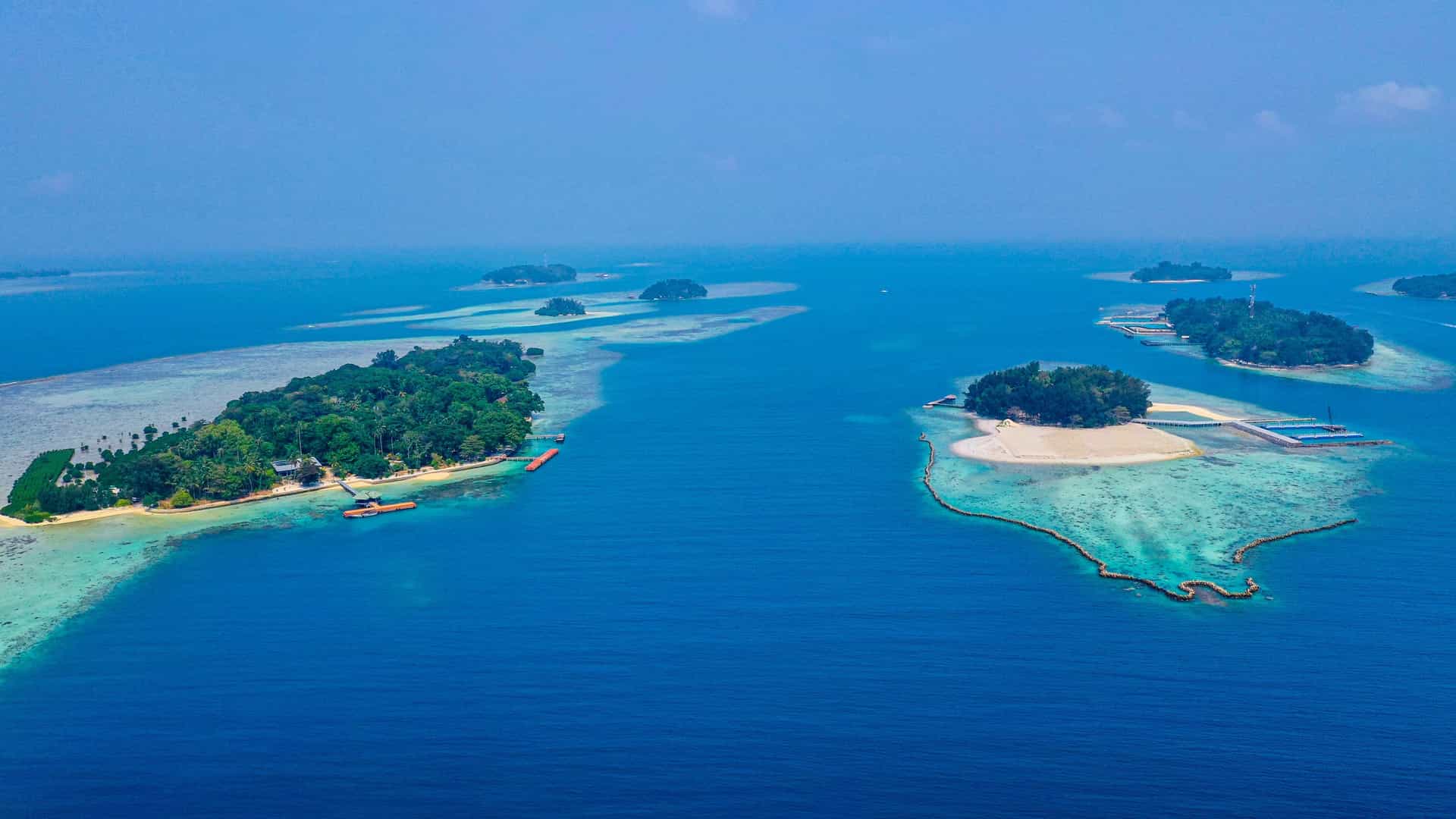 An aerial view of small, tropical islands surrounded by a stunning coral reef and calm, crystal-clear turquoise water in the Java Sea.