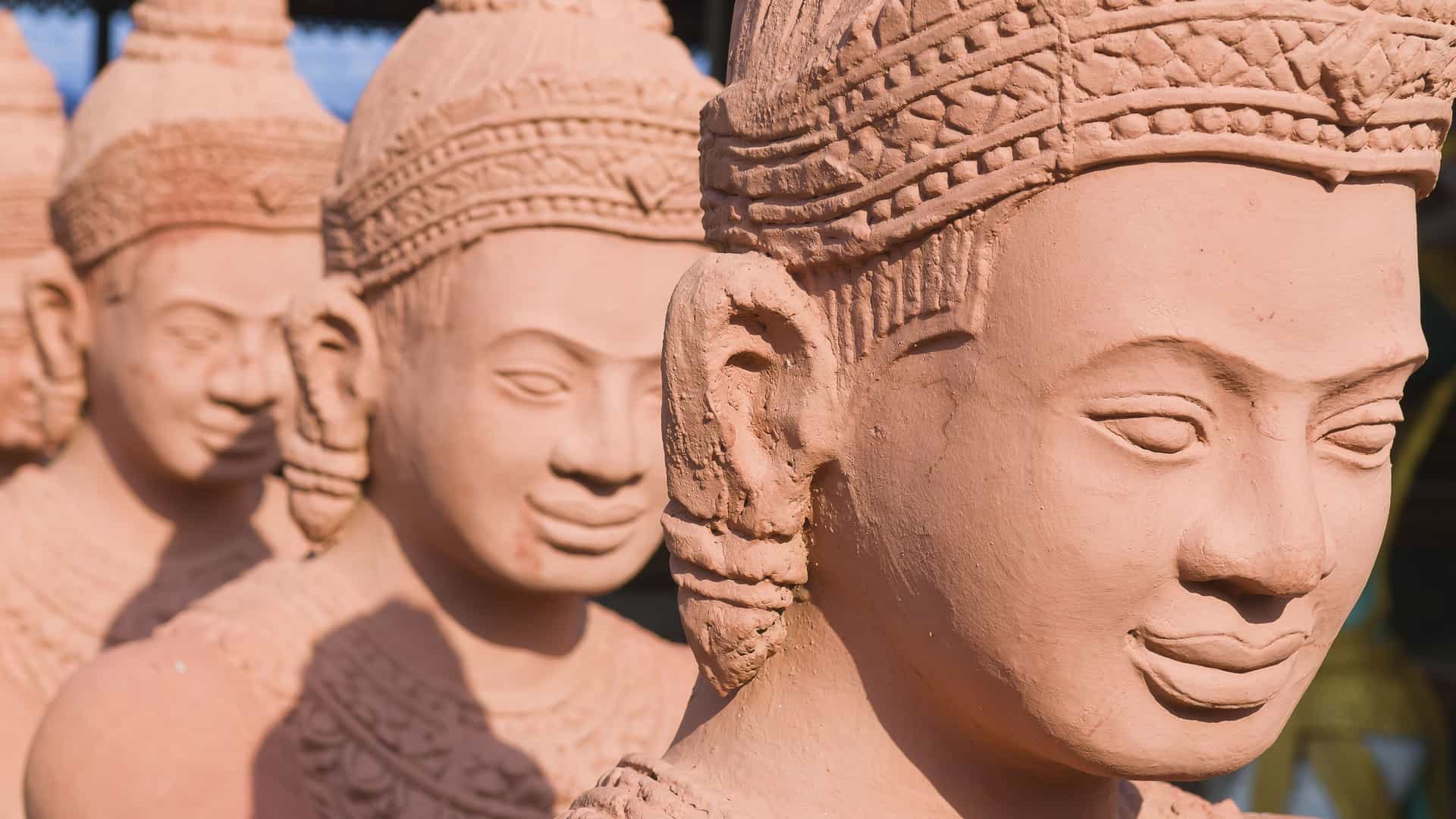 A close-up side view of a row of traditional Cambodian terracotta statues, depicting serene faces with intricate headdresses, a common sight in the art and culture of Kampong Cham.