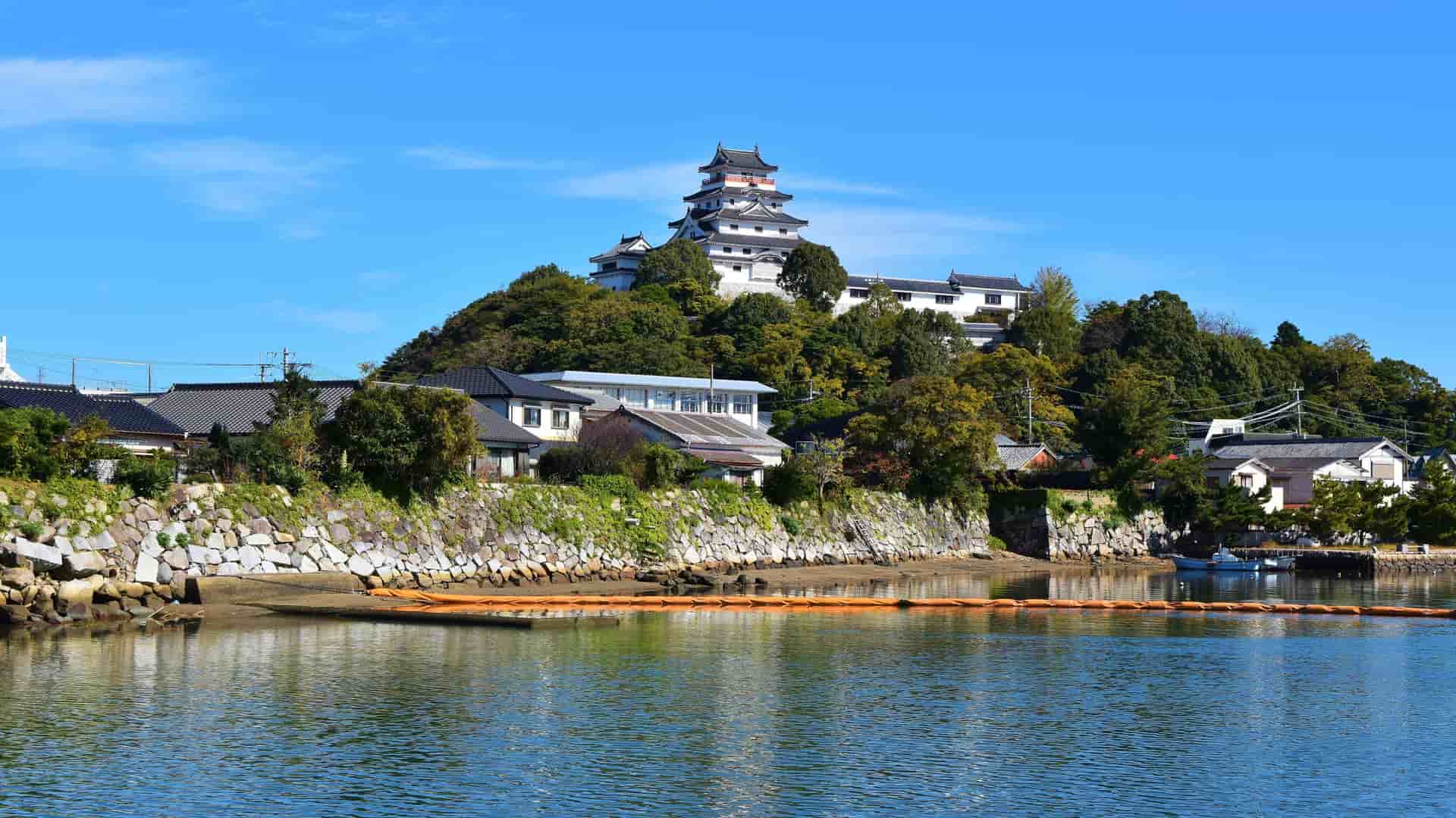A picturesque view of the majestic Karatsu Castle perched on a hill, overlooking the waterfront and traditional Japanese houses in the city of Karatsu, Japan.