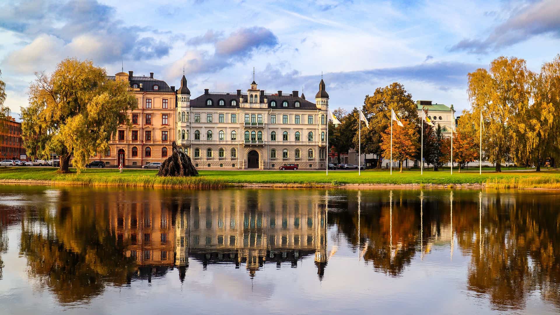 "A scenic autumn shot of the historic Värmlands Museum, a large white building with a castle-like design, reflecting beautifully in the waters of the Klarälven River in Karlstad, Sweden. "