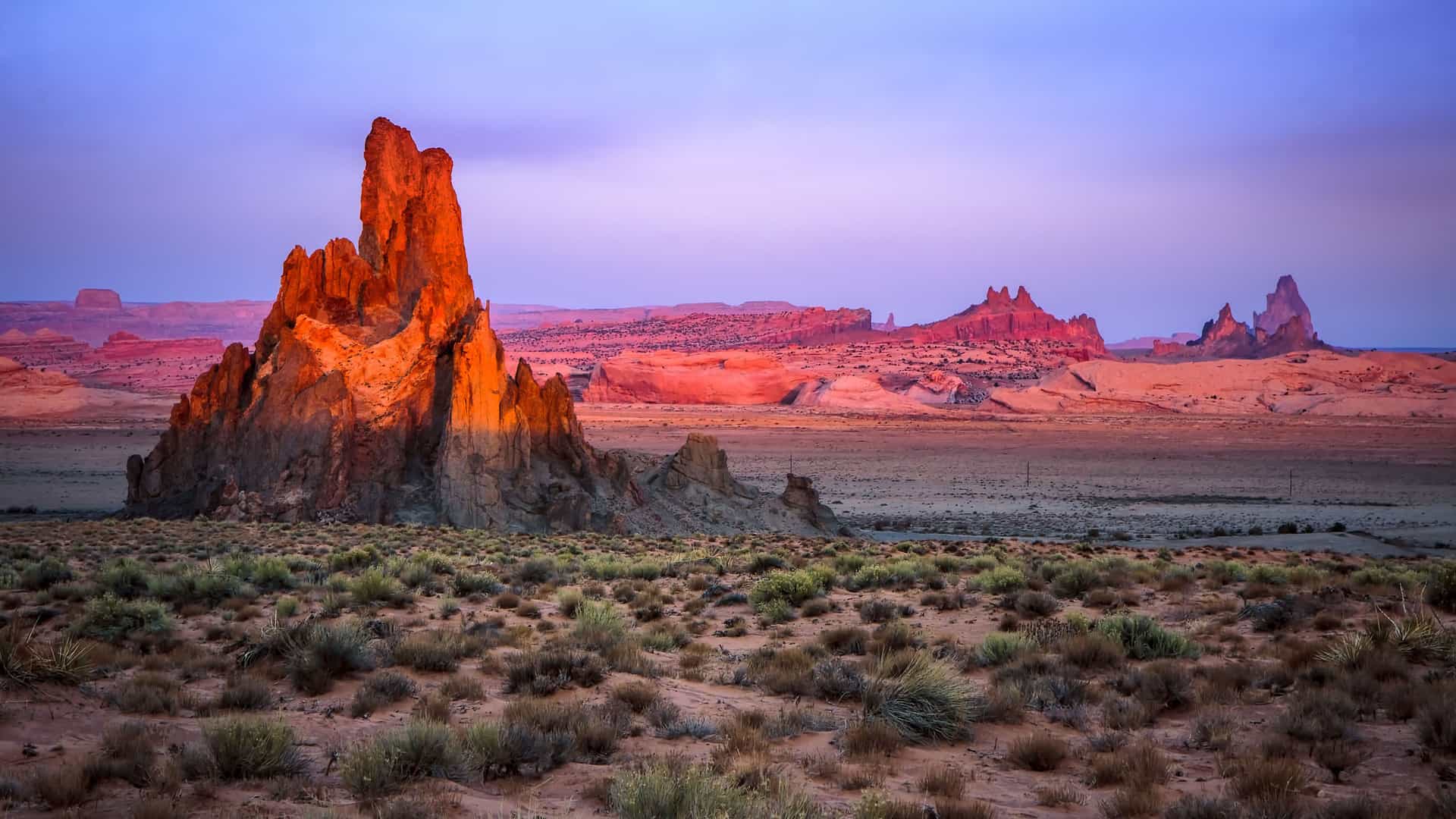 "A beautiful golden-hour shot of Monument Valley, near Kayenta, Arizona, with a striking red rock formation in the foreground and the expansive, arid desert landscape under a colorful sky. "