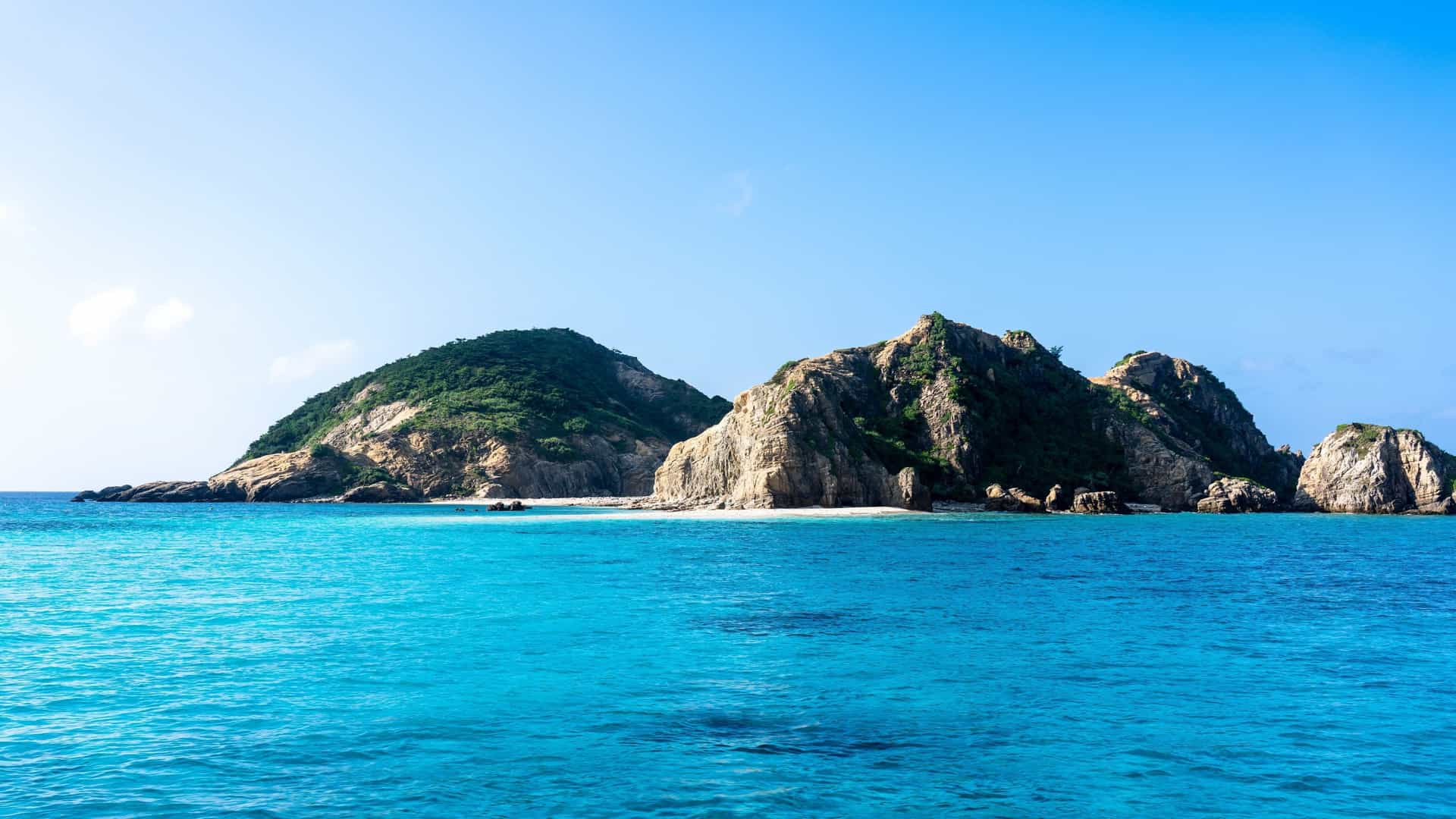 Lush, rocky green islands rise from the intensely blue and turquoise waters of the Kerama Islands, Japan.