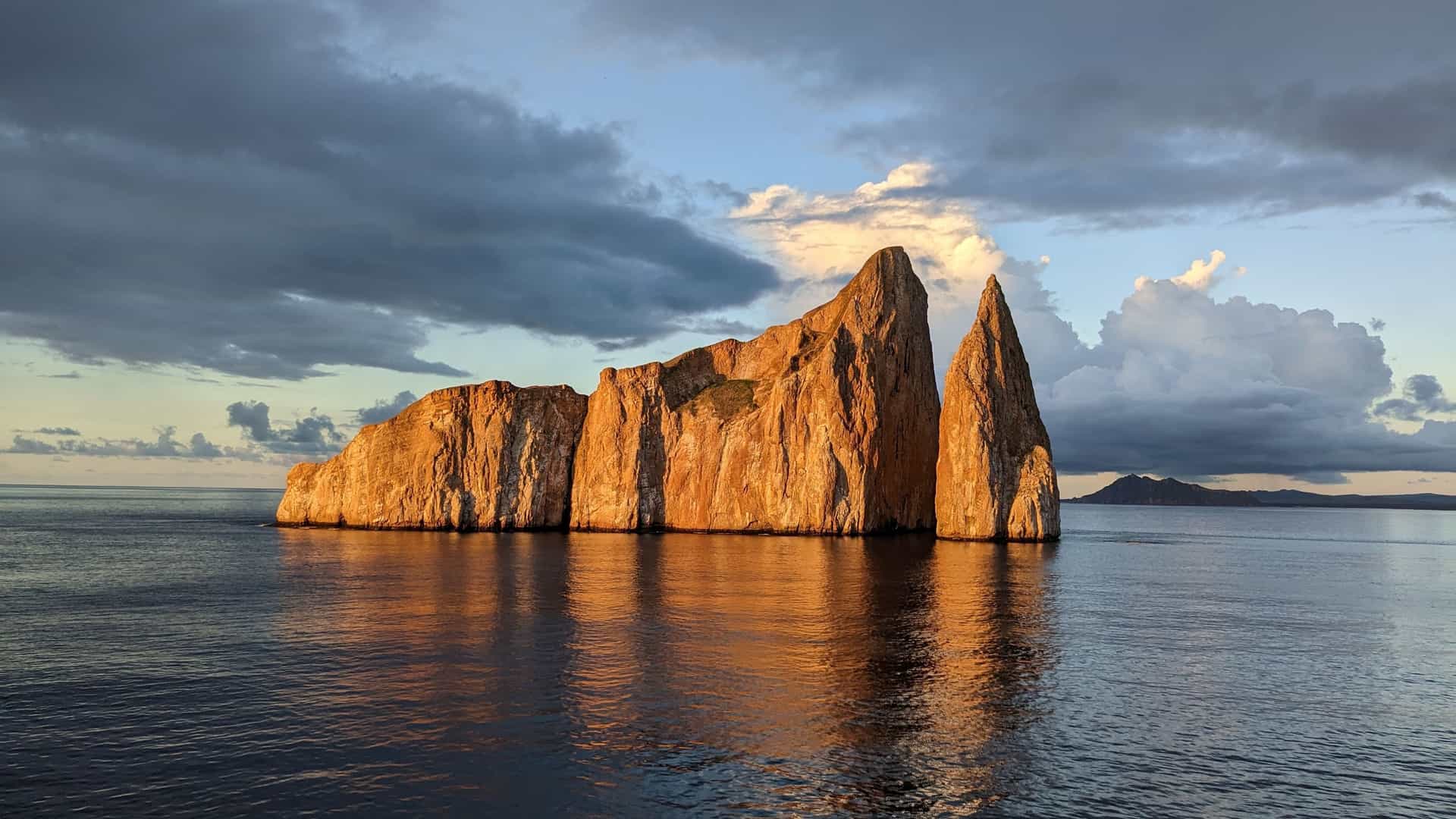 Kicker Rock in the Galapagos Islands, a large volcanic rock formation with two peaks rising from the calm ocean, lit by the warm glow of the setting sun.