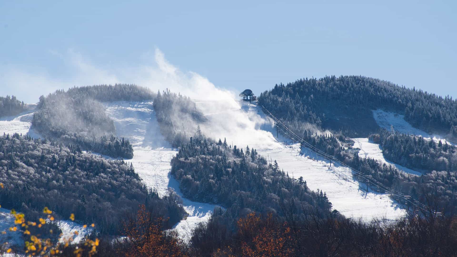 "A snowy scene of the Killington ski resort in Vermont, showing a ski lift ascending a snow-covered mountain with snow machines blowing artificial snow onto the trails. "
