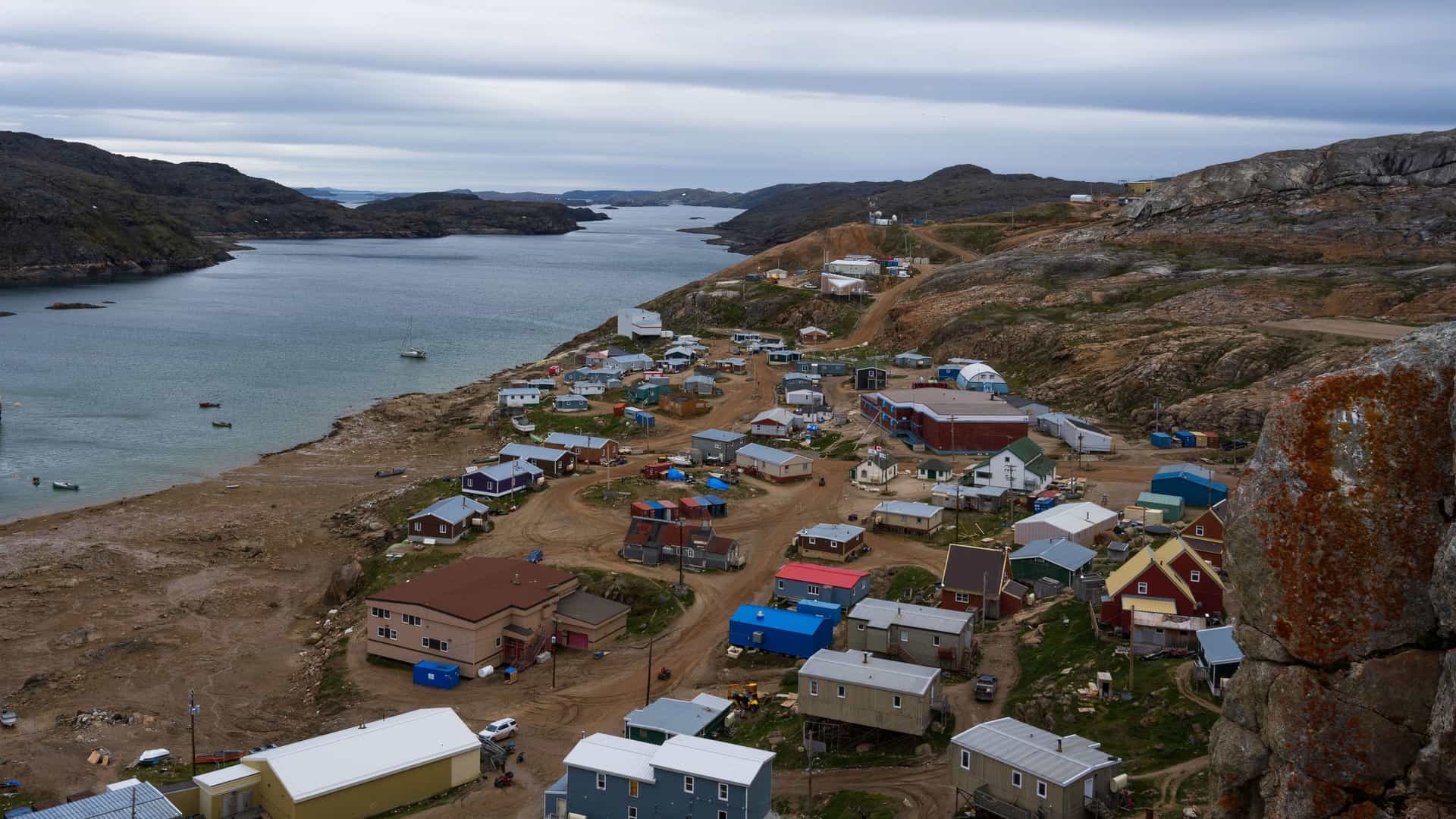 An aerial view of Kimmirut, a remote Inuit community in Nunavut, Canada, with colorful houses scattered along a rocky coastline next to a bay and surrounded by treeless hills.