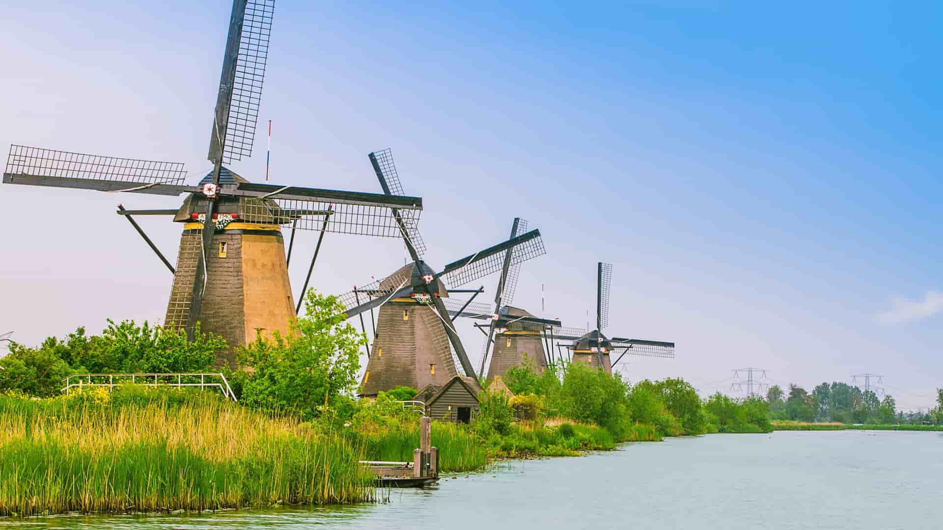 A row of historic thatched-roof windmills stand along the tranquil canal at Kinderdijk, Netherlands, a UNESCO World Heritage site and popular tourist destination.