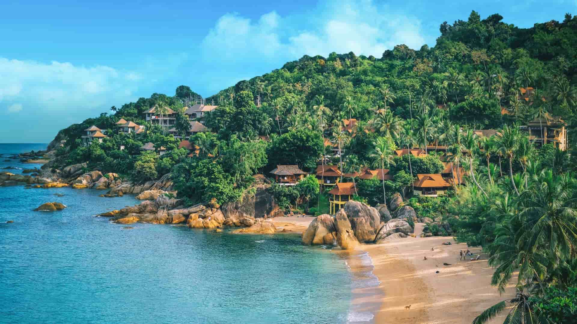 A breathtaking panoramic view of a secluded cove in Koh Samui, Thailand, with a sandy beach and luxury resorts nestled in lush green tropical forests and palm trees.