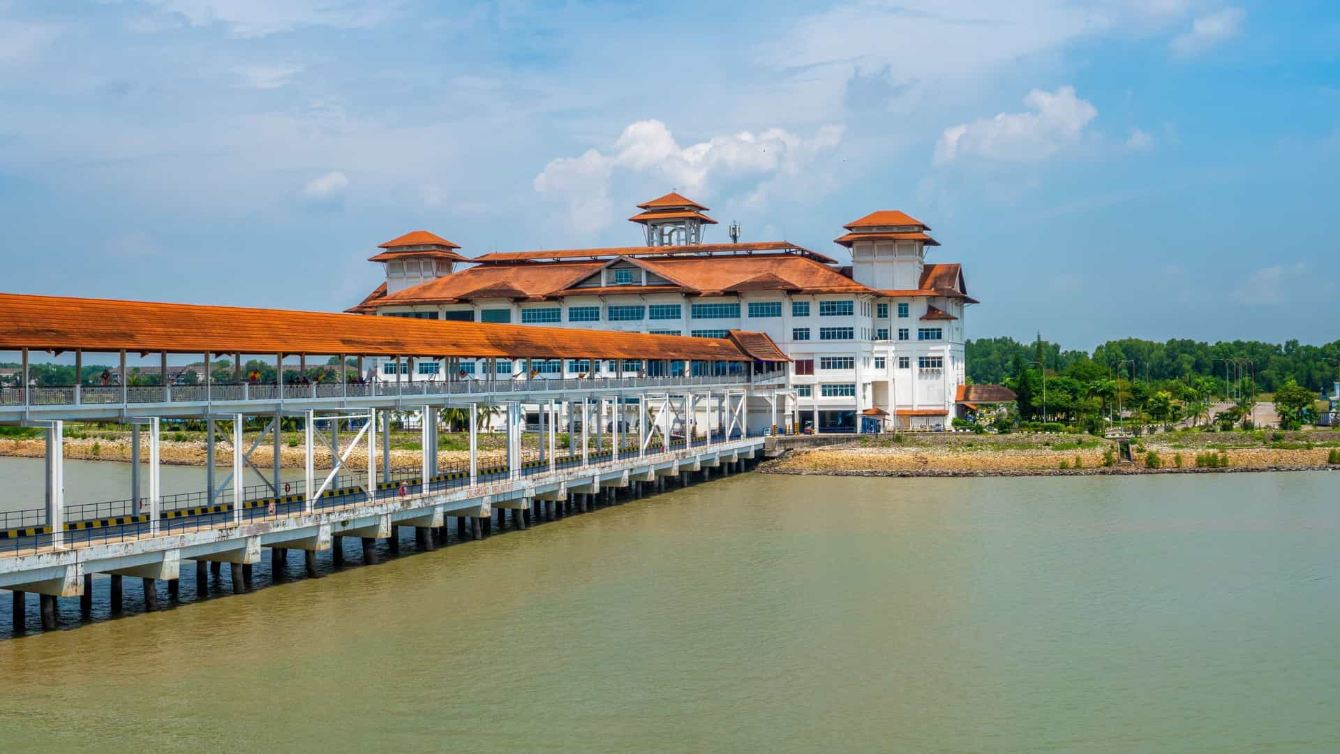 A view of the main cruise terminal building at Port Klang in Kuala Lumpur, Malaysia, with its unique architectural style, a long covered walkway, and the sea in front.