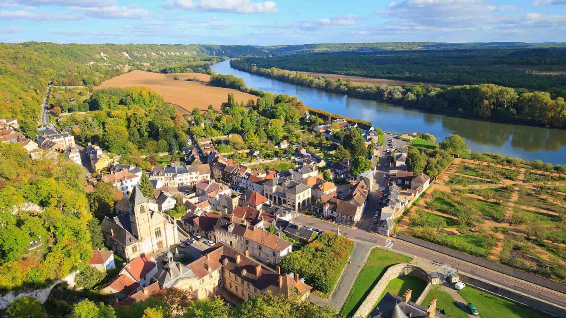 An aerial view of La Roche-Guyon, a picturesque French village nestled on the banks of the winding Seine River, surrounded by lush green hills.