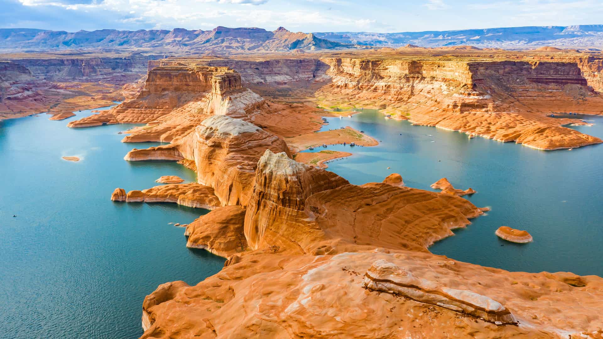 "An aerial panoramic shot of Lake Powell, a beautiful man-made reservoir in Utah, showcasing its vibrant blue waters and the stunning contrast of the red sandstone cliffs and unique rock formations. "