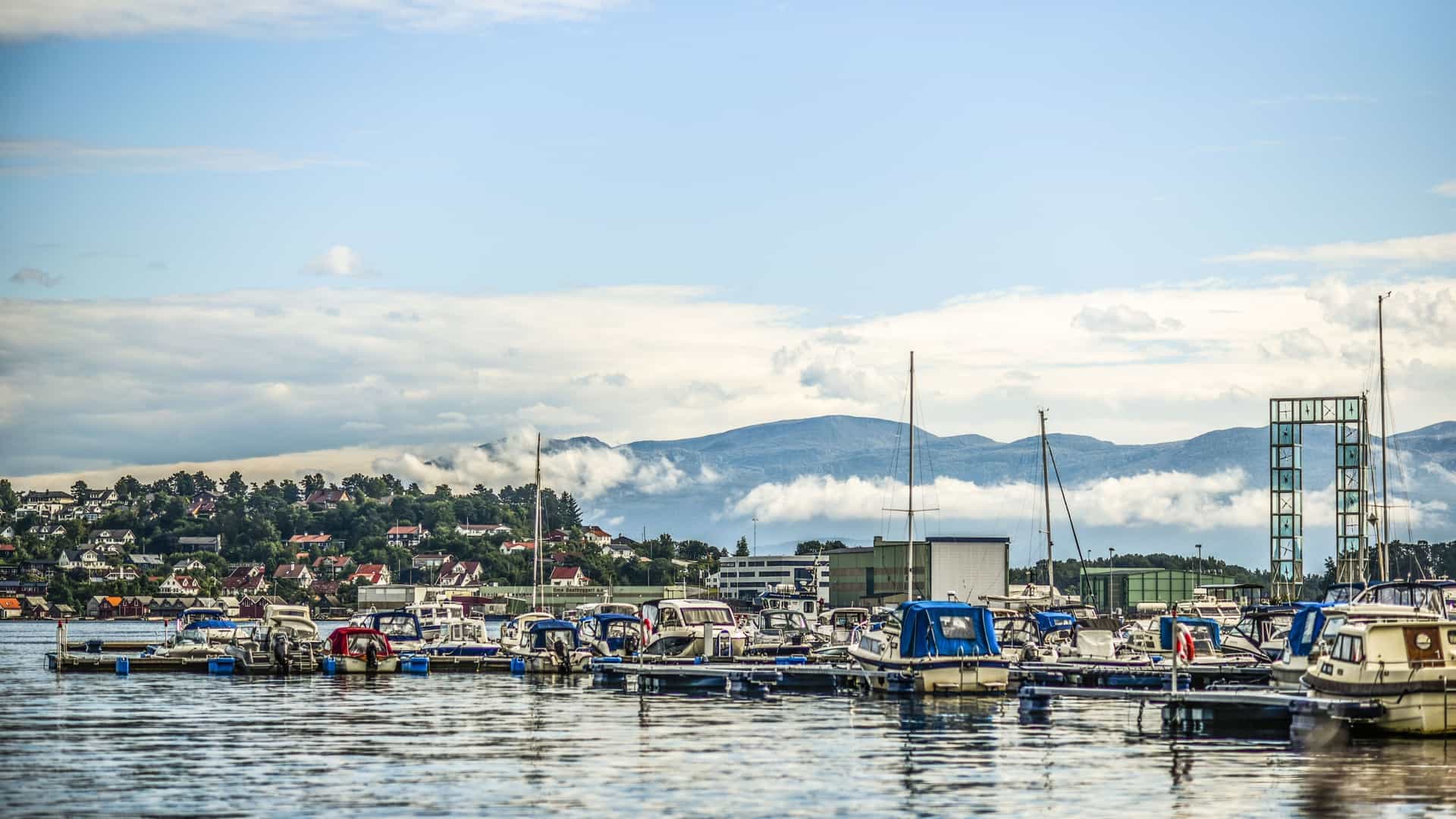 A harbor view of Leirvik, Norway, with boats docked in the foreground, and the town's residential area climbing up a hill towards the mountains in the background.