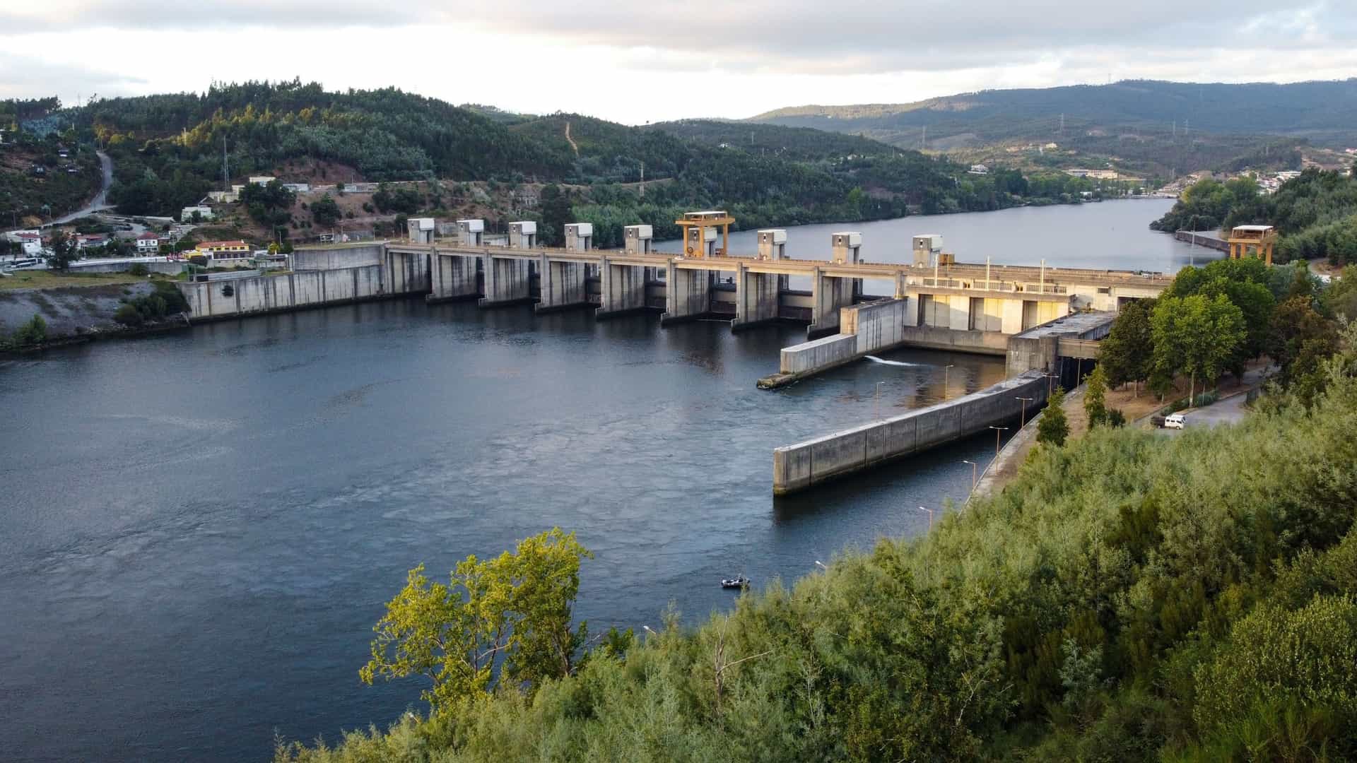 A panoramic view of the Carrapatelo Dam and Lock on the Douro River in Portugal, with the hydroelectric facility stretching across the wide river surrounded by lush, green hills.