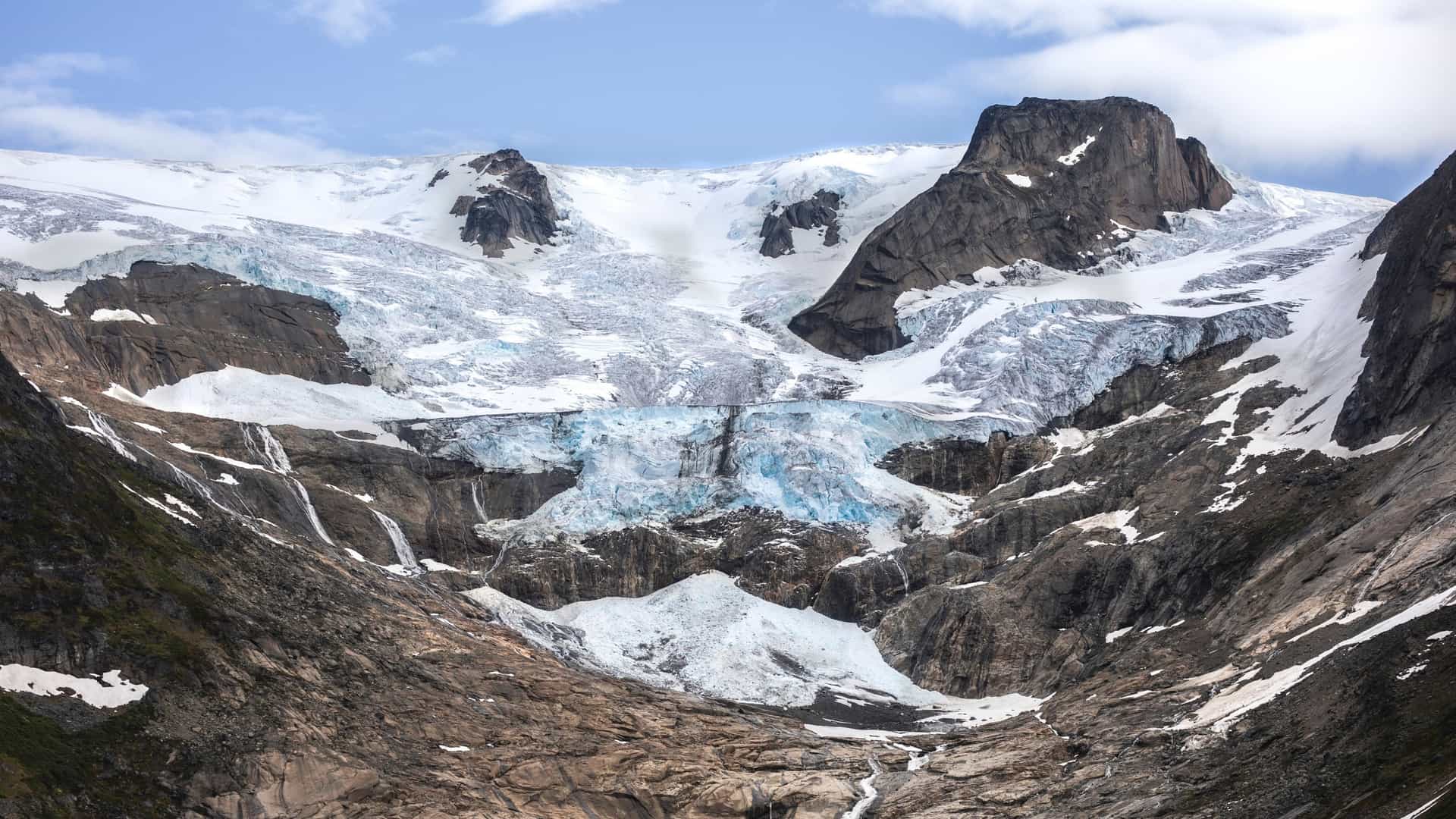 A dramatic, dark blue glacier clings to the high, rugged rock walls of Lindenow Fjord, Greenland.