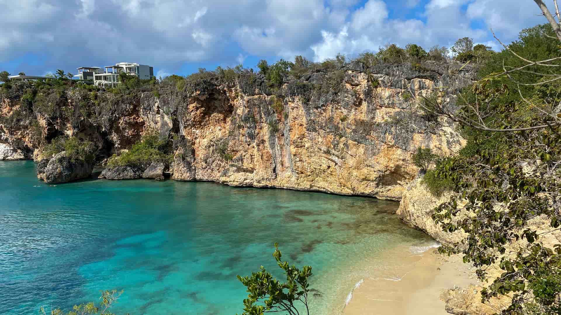 A stunning image of Little Bay in Anguilla, a secluded, beautiful beach with turquoise water surrounded by towering rocky cliffs and lush green vegetation.