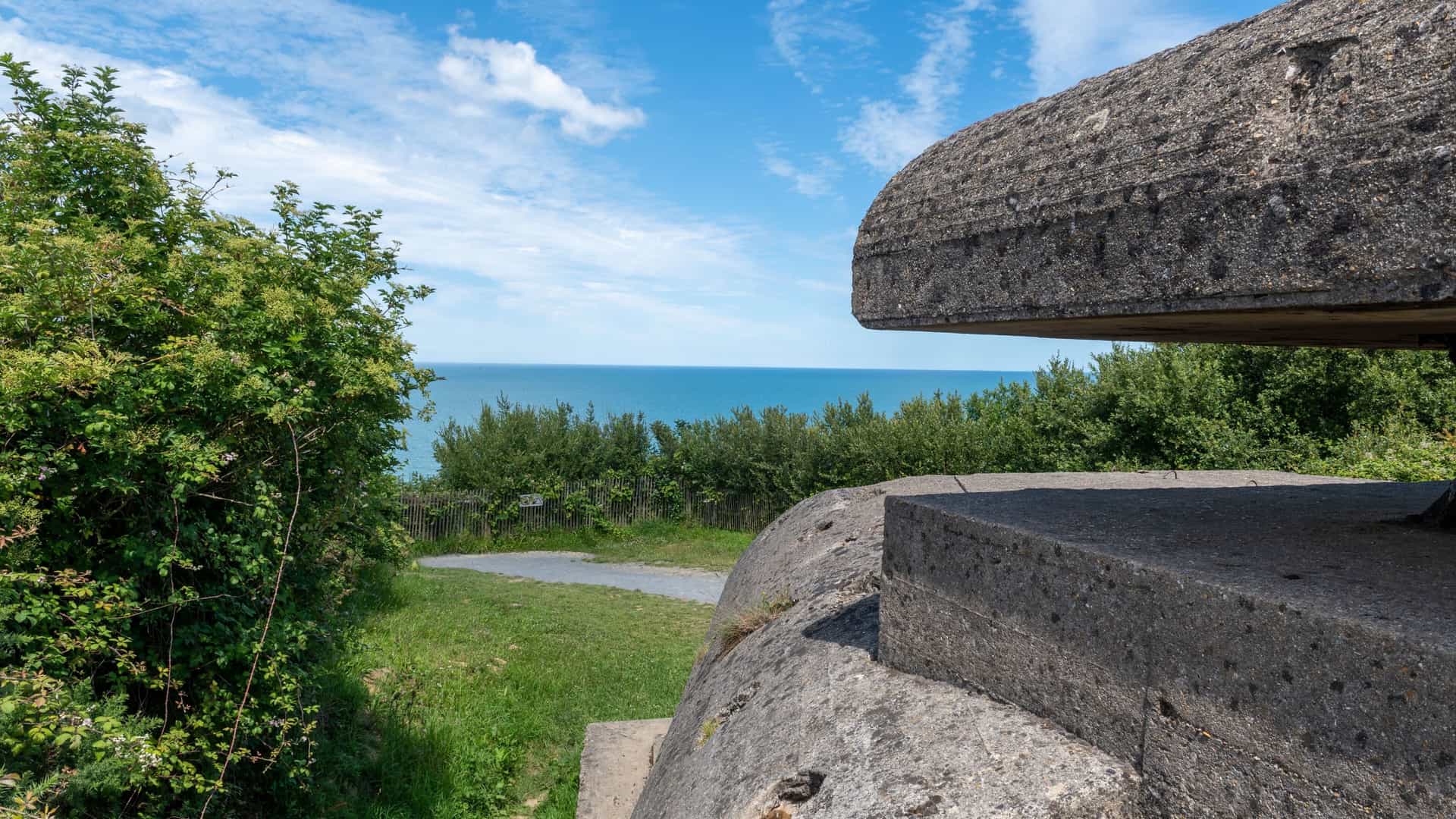 A concrete German bunker from World War II overlooking the calm waters of the English Channel at Longues-sur-Mer, a historical landmark on the Normandy coast.