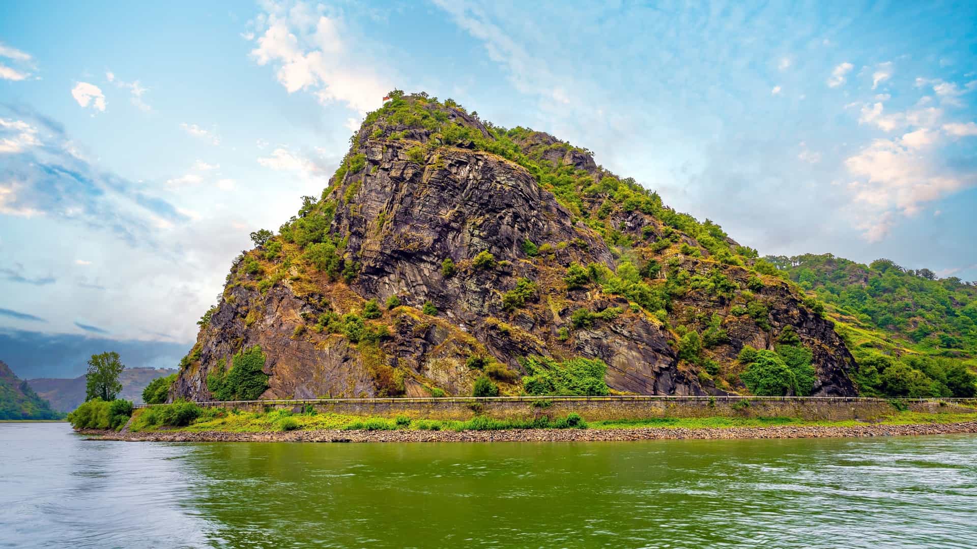 The massive, steep Lorelei Rock on the Rhine River near Sankt Goarshausen, Germany, rises dramatically above the green water.