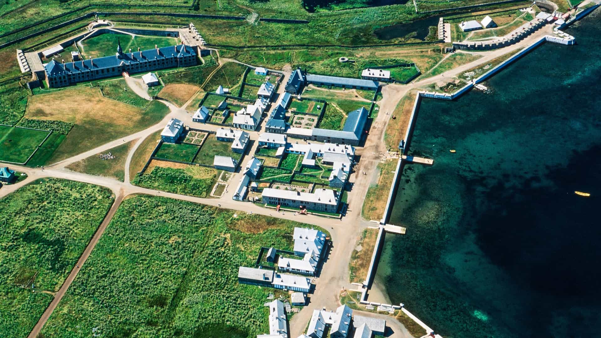 An aerial view of the Fortress of Louisbourg, a historical reconstruction of a French fortification, showing its extensive buildings, gardens, and harbor on Cape Breton Island, Nova Scotia.
