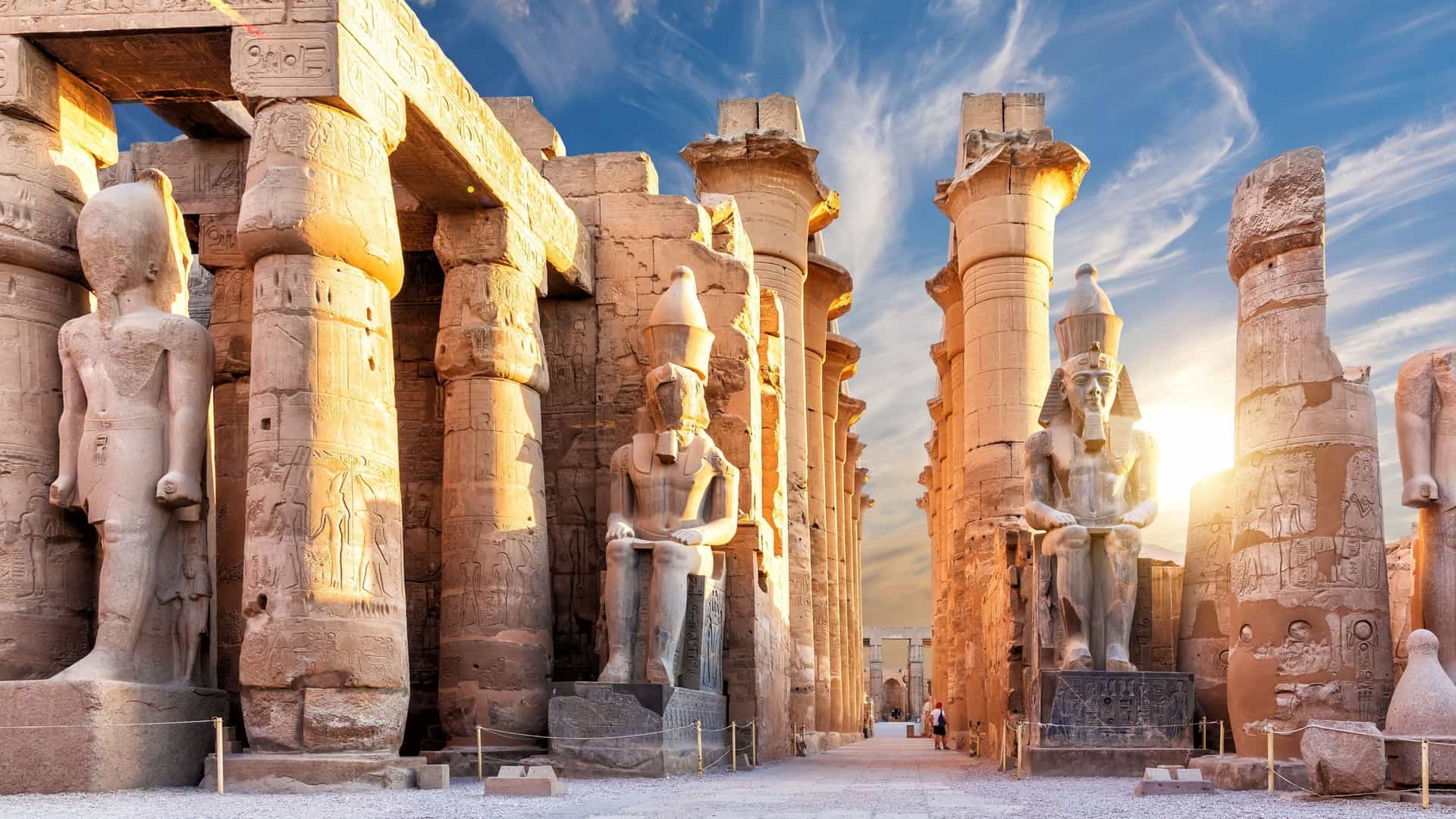 A breathtaking sunset view of the ancient Luxor Temple in Egypt, showcasing towering statues of pharaohs, massive columns, and hieroglyphics bathed in golden light.